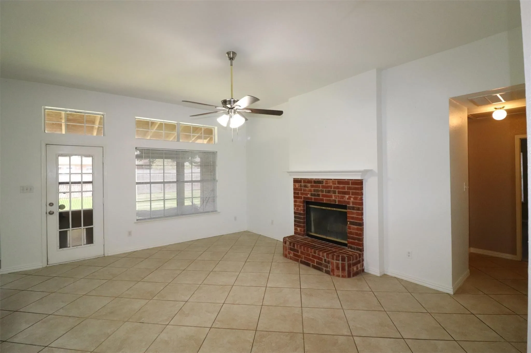 Brick fireplace with hearth, ceiling fan with light fixture, tiled flooring, and multiple windows