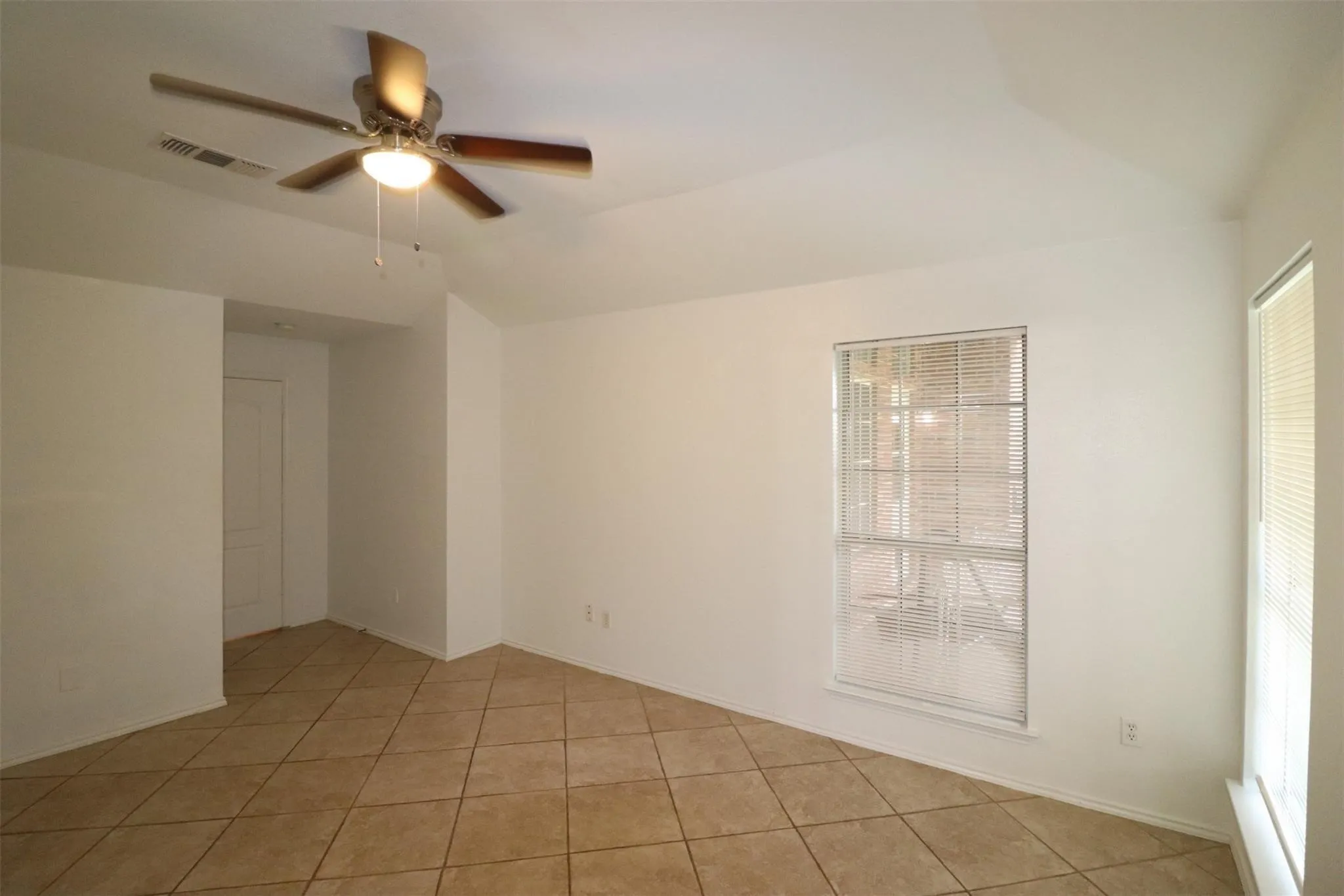 Neutral-toned ceramic tile flooring, vaulted ceiling, and dual windows with blinds