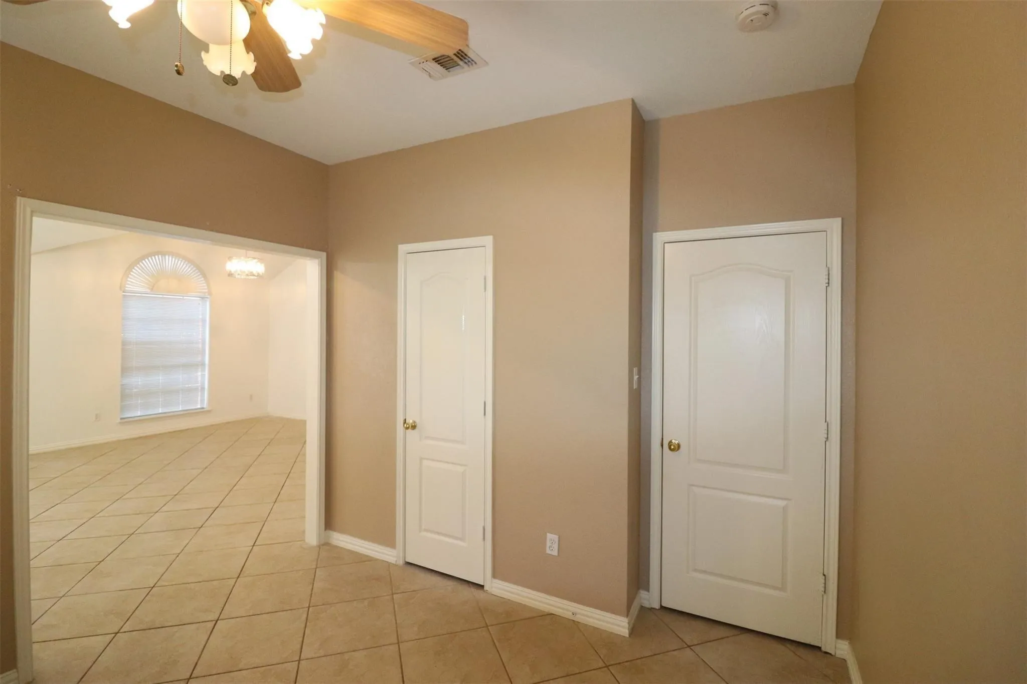 Open archway, neutral painted walls, tiled flooring, ceiling fan with light fixture, and white paneled doors