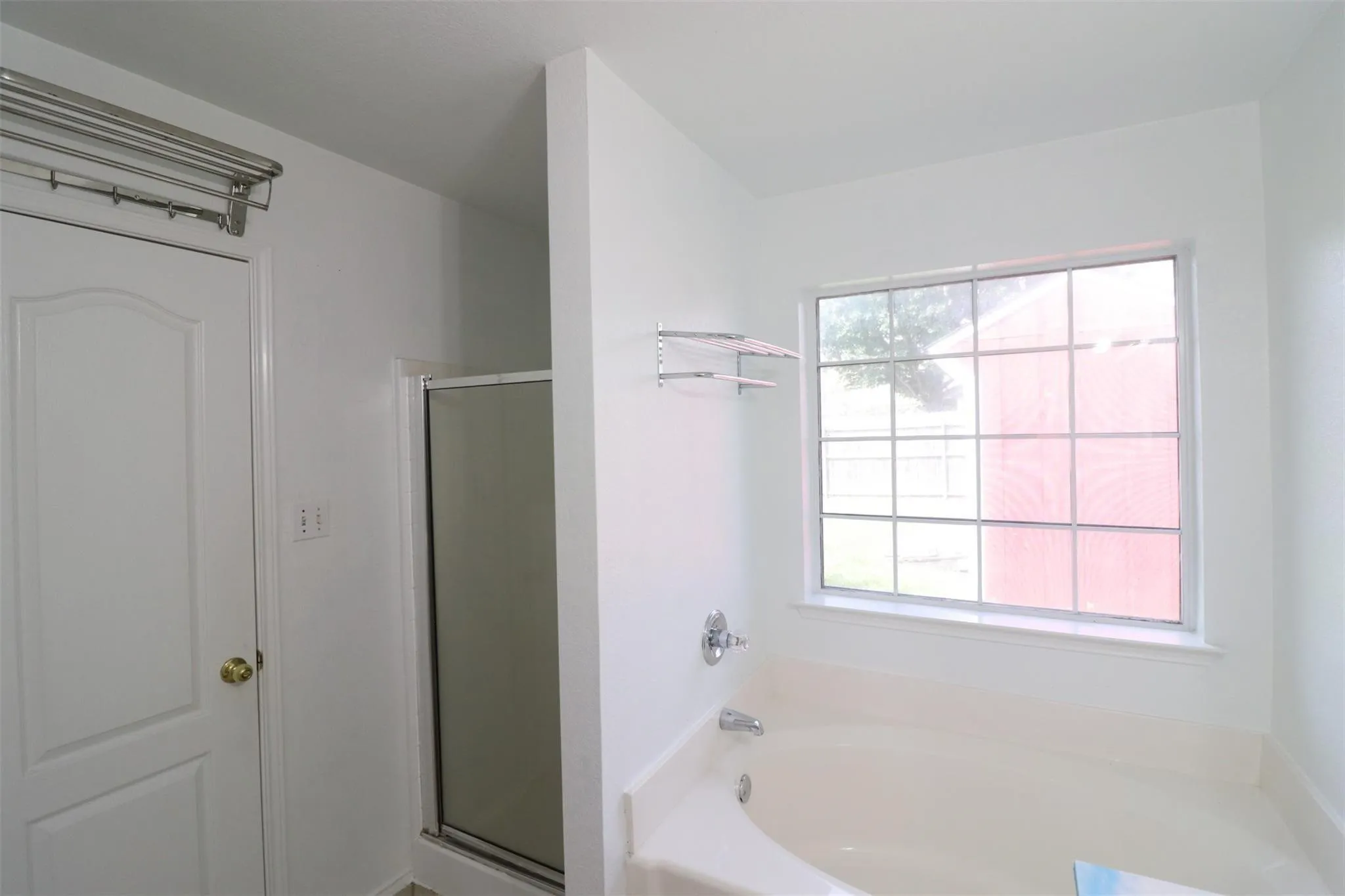 Soaking tub with chrome fixtures, fixed pane window, shower enclosure with glass door, and a white paneled door