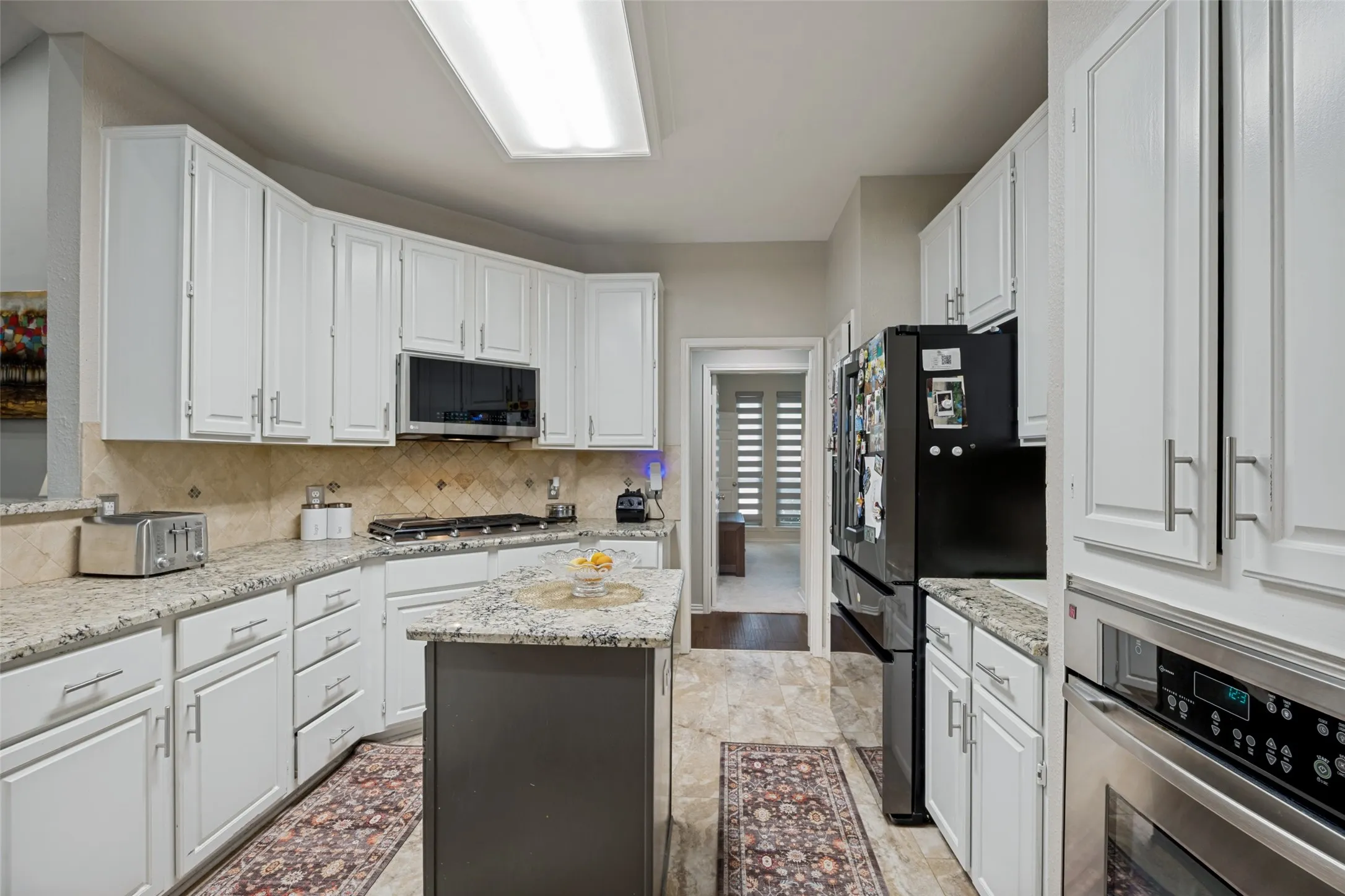 Galley kitchen featuring white cabinetry, granite countertops, tile backsplash, and stainless steel built-in appliances