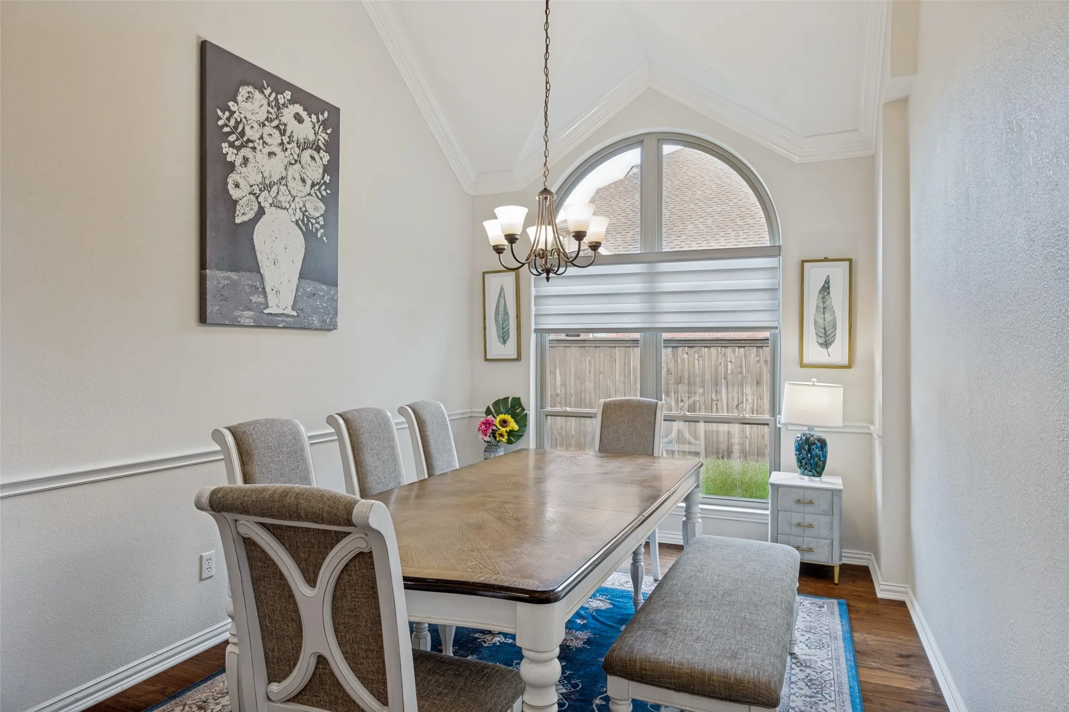 Vaulted ceiling with crown molding, elegant chandelier, arched window, wood-finish flooring, and chair rail molding