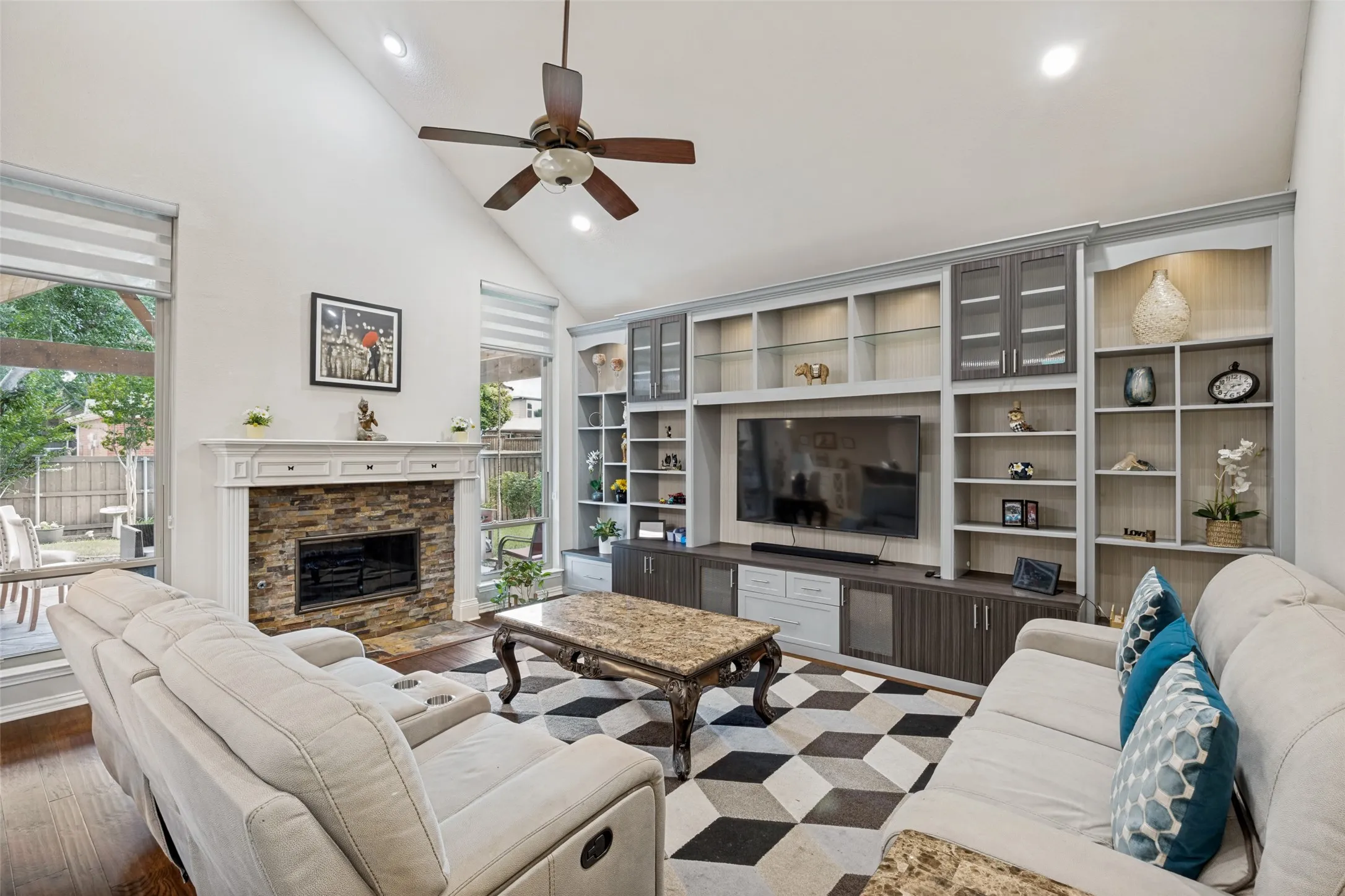 Vaulted ceiling, built-in entertainment center, stone-faced fireplace with white mantel, recessed lighting, and wood-finish flooring
