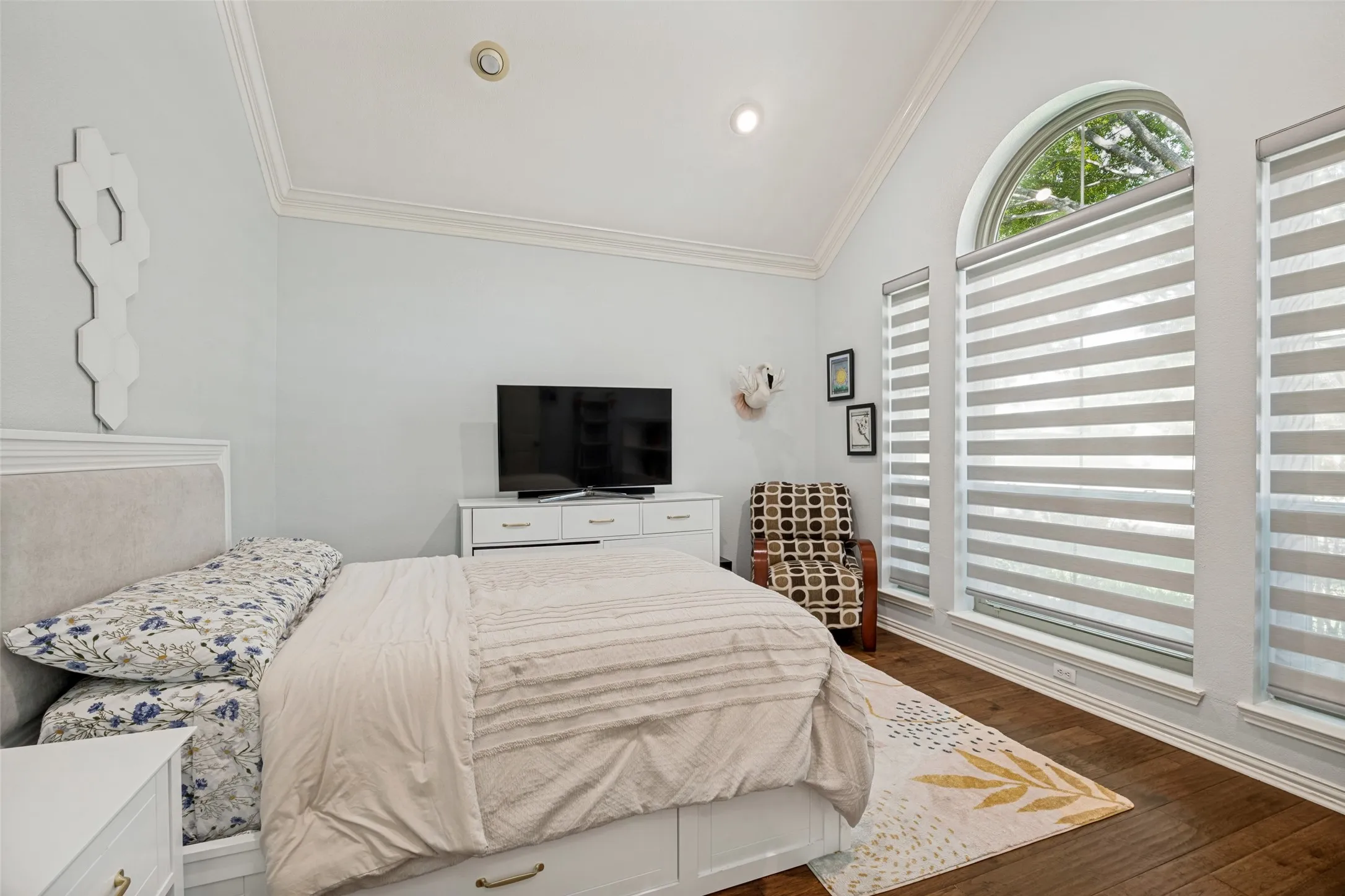 Vaulted ceiling with crown molding, arched top window, wood-finish flooring, and crisp white trim