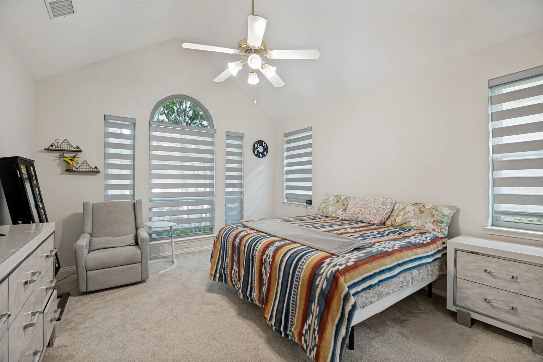 Vaulted ceiling with a ceiling fan, arched window, three additional windows, and carpeted flooring
