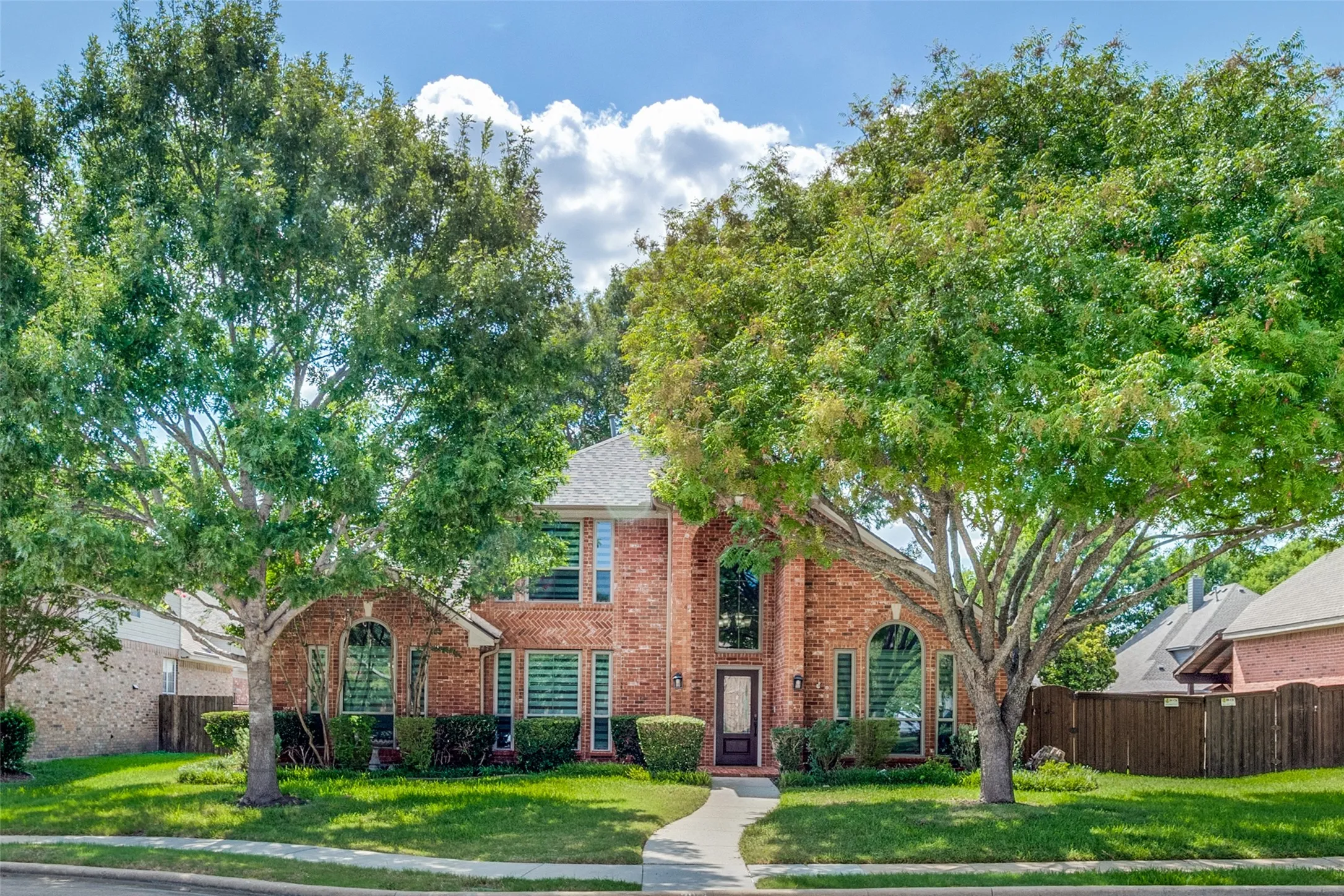 Brick exterior with arched window details, a prominent entry, and a gabled roofline, complemented by mature trees and a concrete pathway