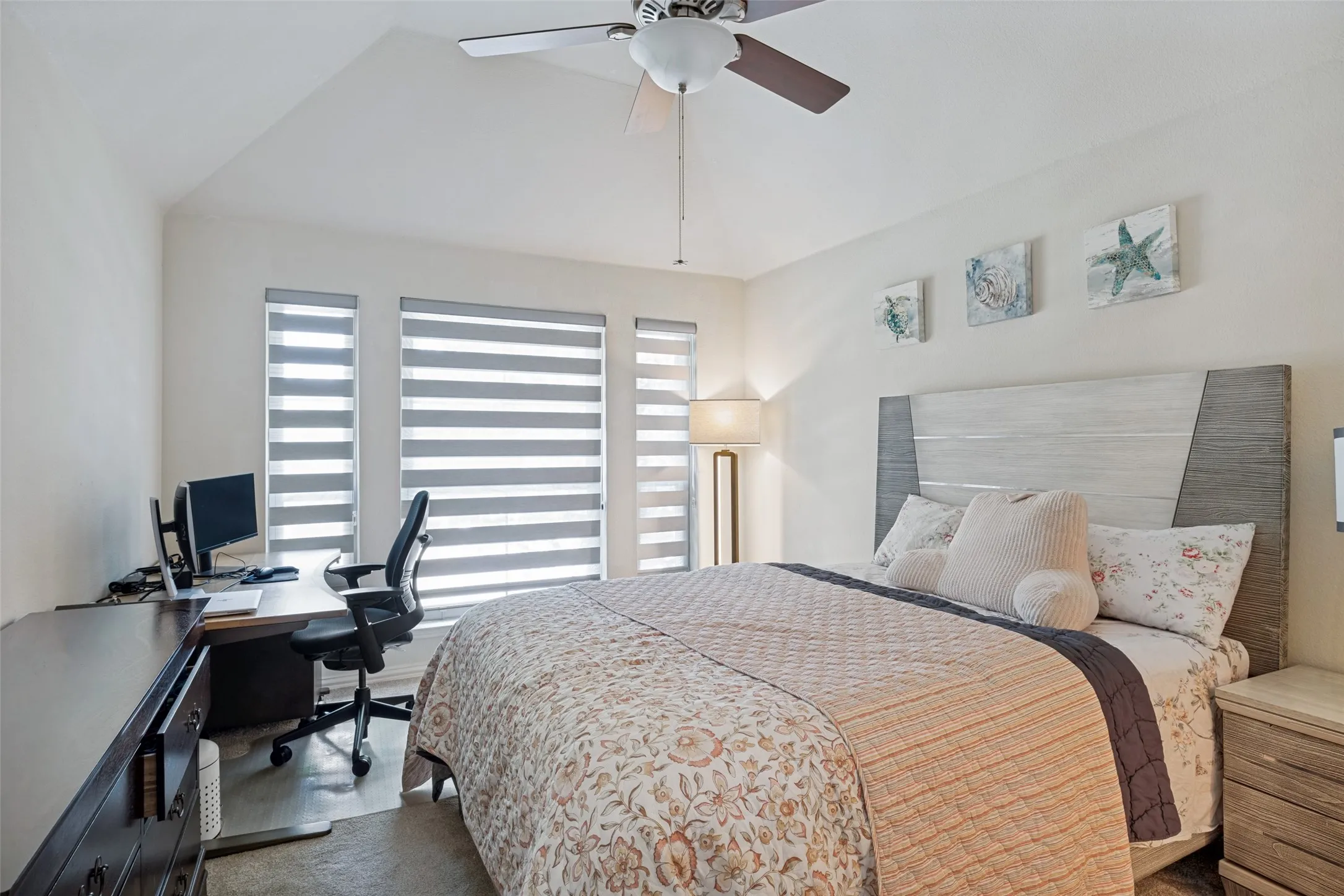 Vaulted ceiling, ceiling fan, multiple windows with blinds, wood-finish headboard, and built-in desk area