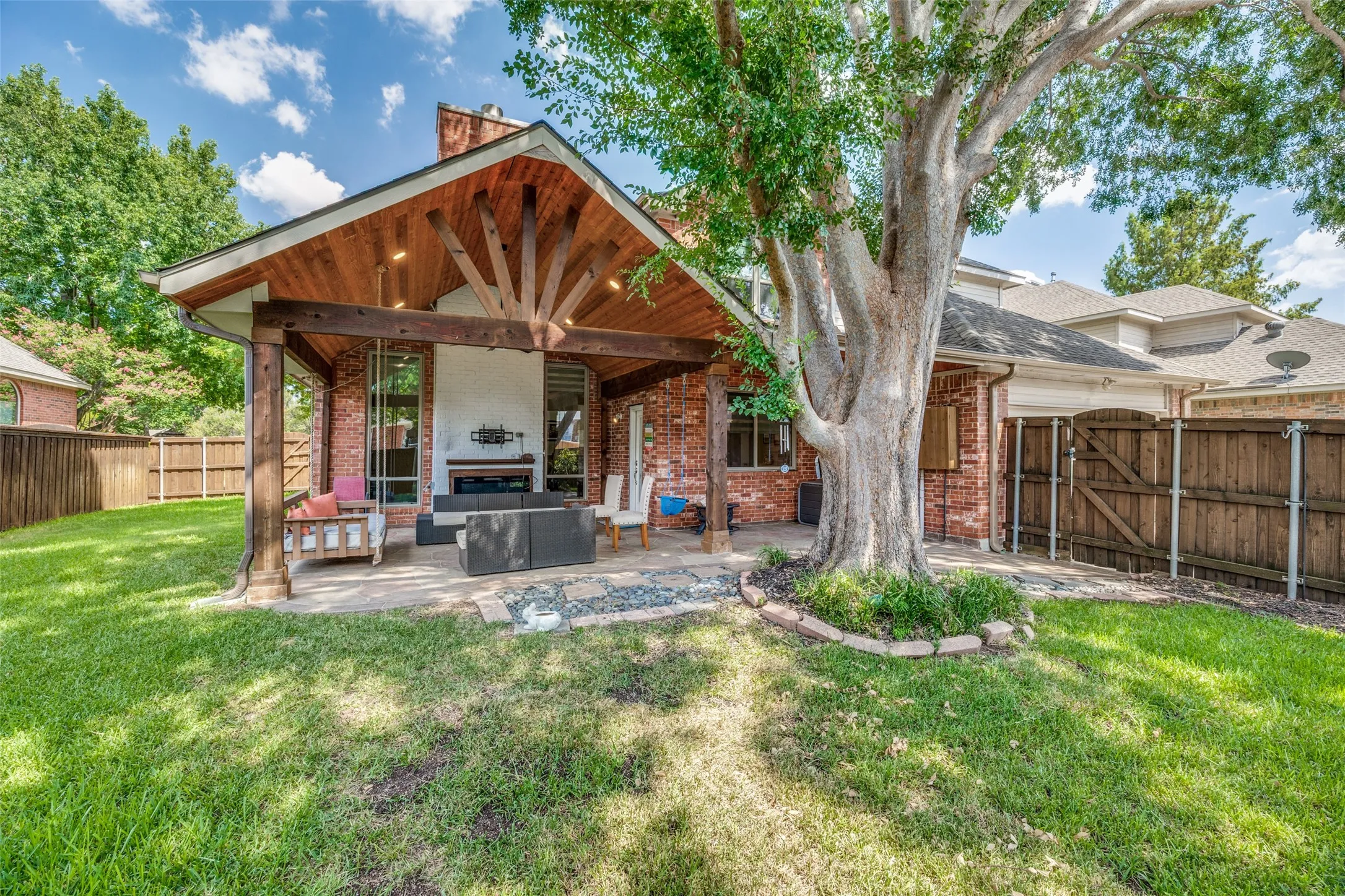 Covered patio with a high vaulted wood-beamed ceiling, brick exterior, and a built-in outdoor fireplace