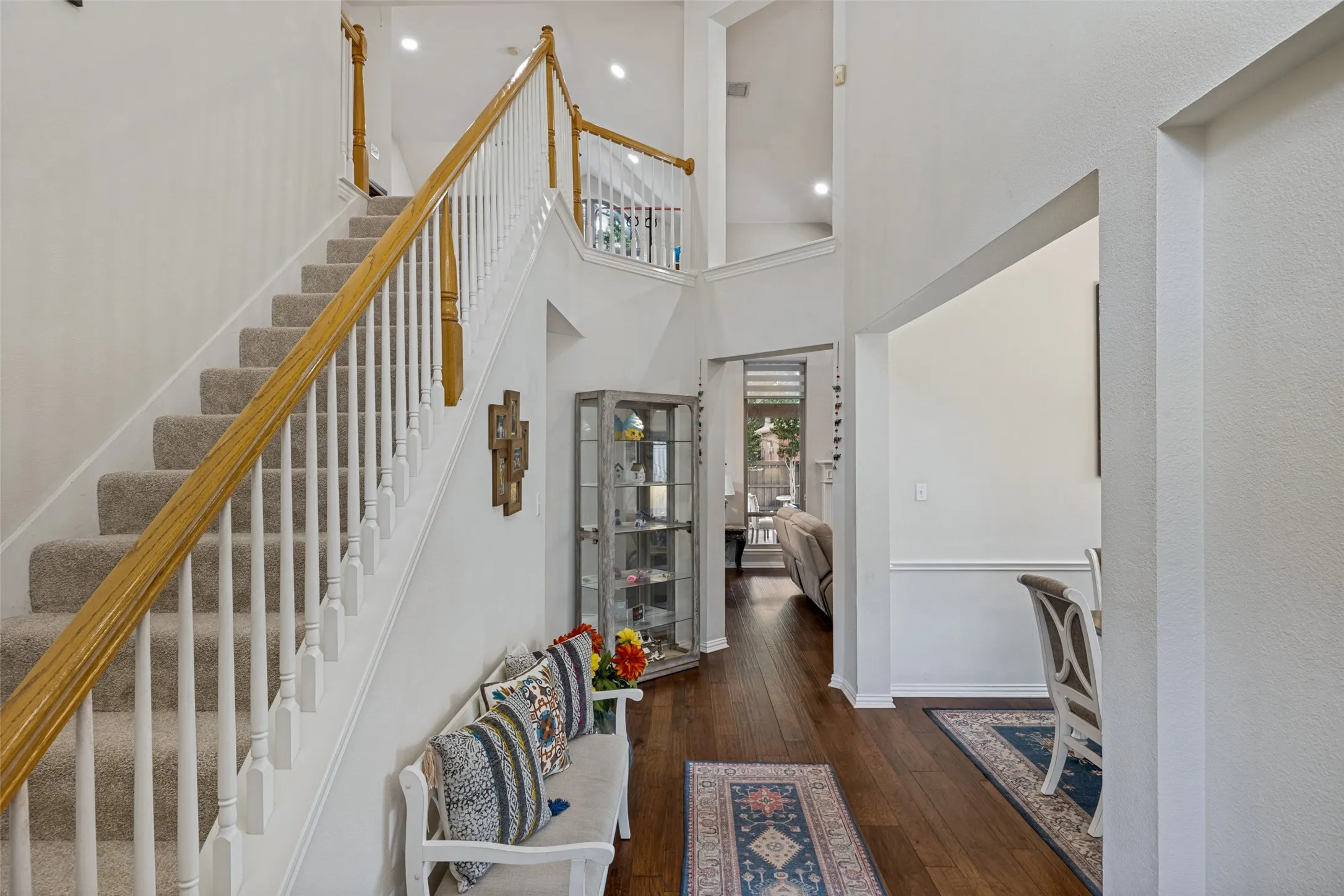 Two-story entry foyer with wood-finish flooring, a carpeted staircase with wood and white balusters, recessed lighting, and a transom window above an exterior door