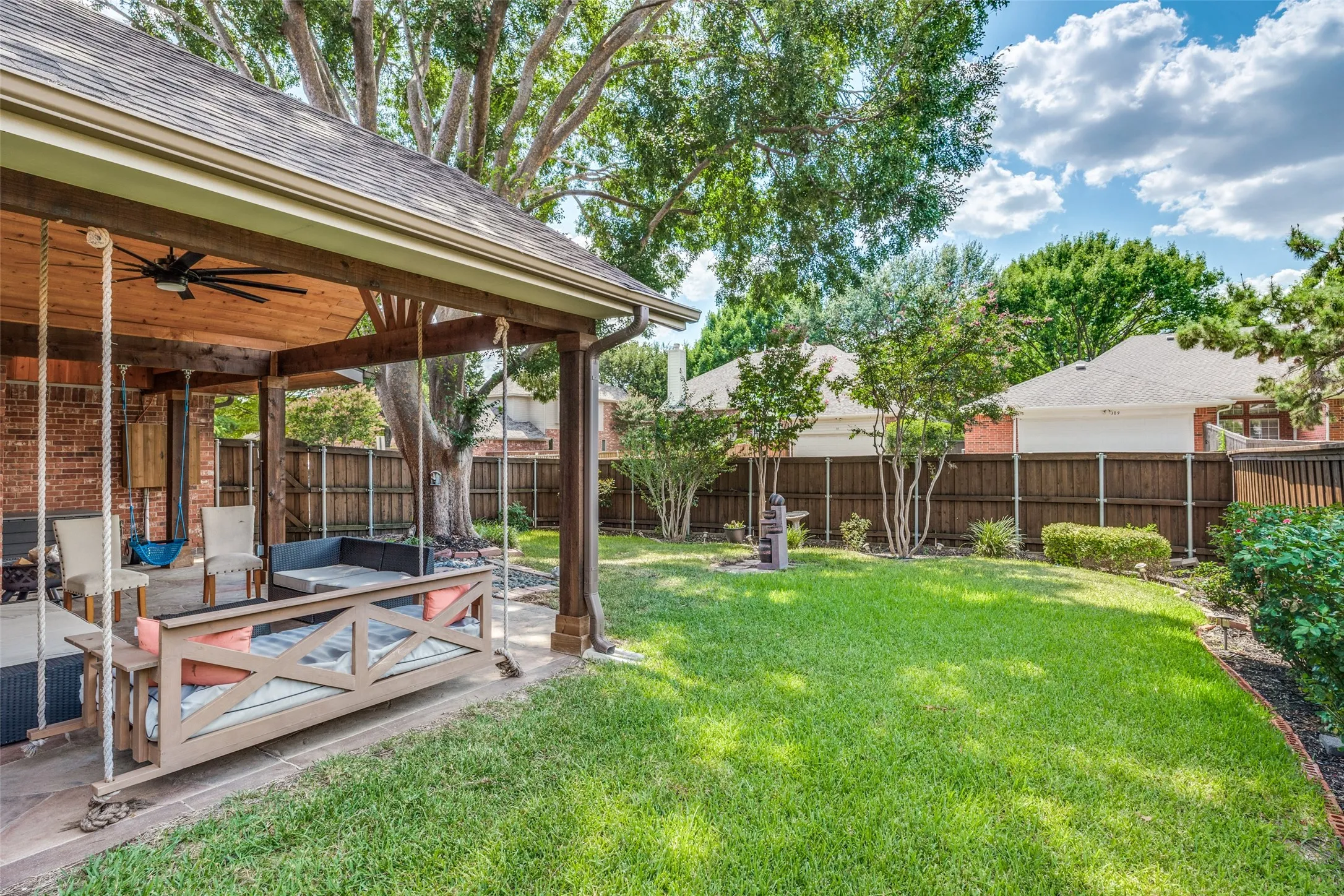 Covered patio with a wood-plank ceiling, ceiling fan, and brick wall