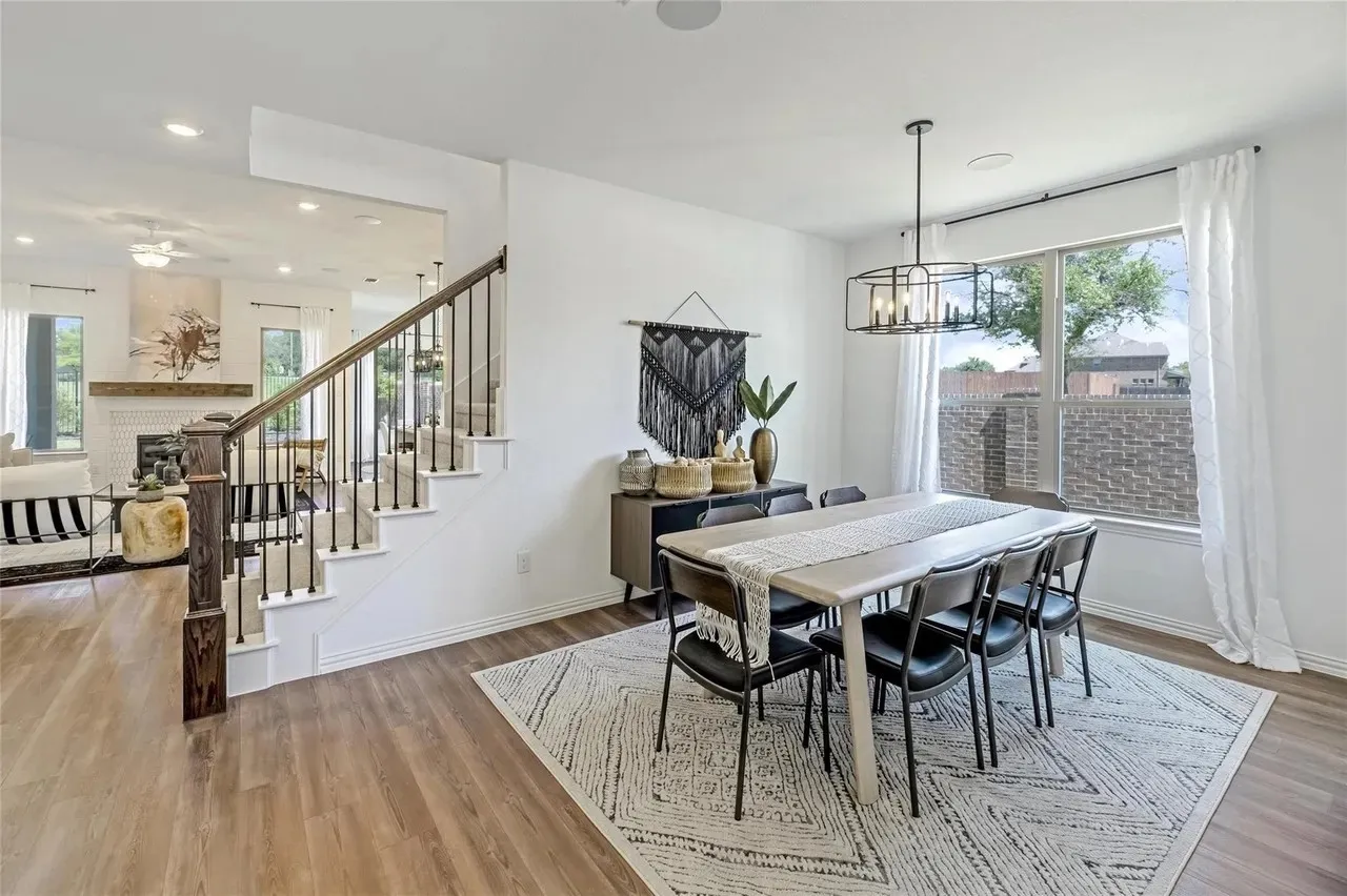 Wood-finish flooring throughout, white walls, staircase with dark wood handrail and black metal balusters, and a window with white curtains