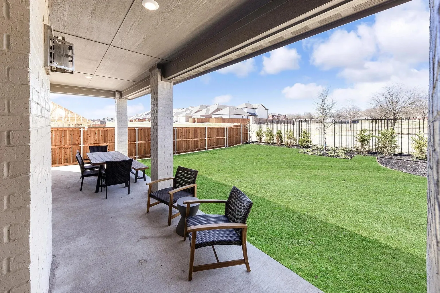 Covered concrete patio with recessed lighting, white brick exterior, and a manicured lawn