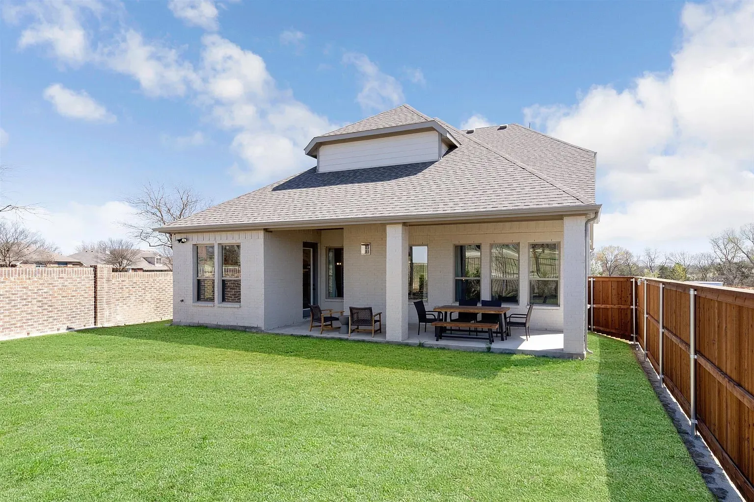 Expansive backyard featuring a manicured lawn, covered patio, multiple windows, and privacy fencing