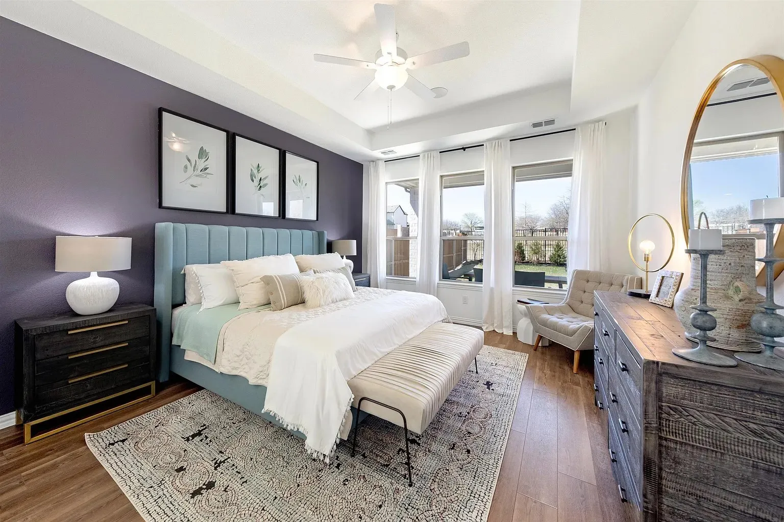 Tray ceiling with a ceiling fan, three large windows, wood-finish flooring, and a feature wall