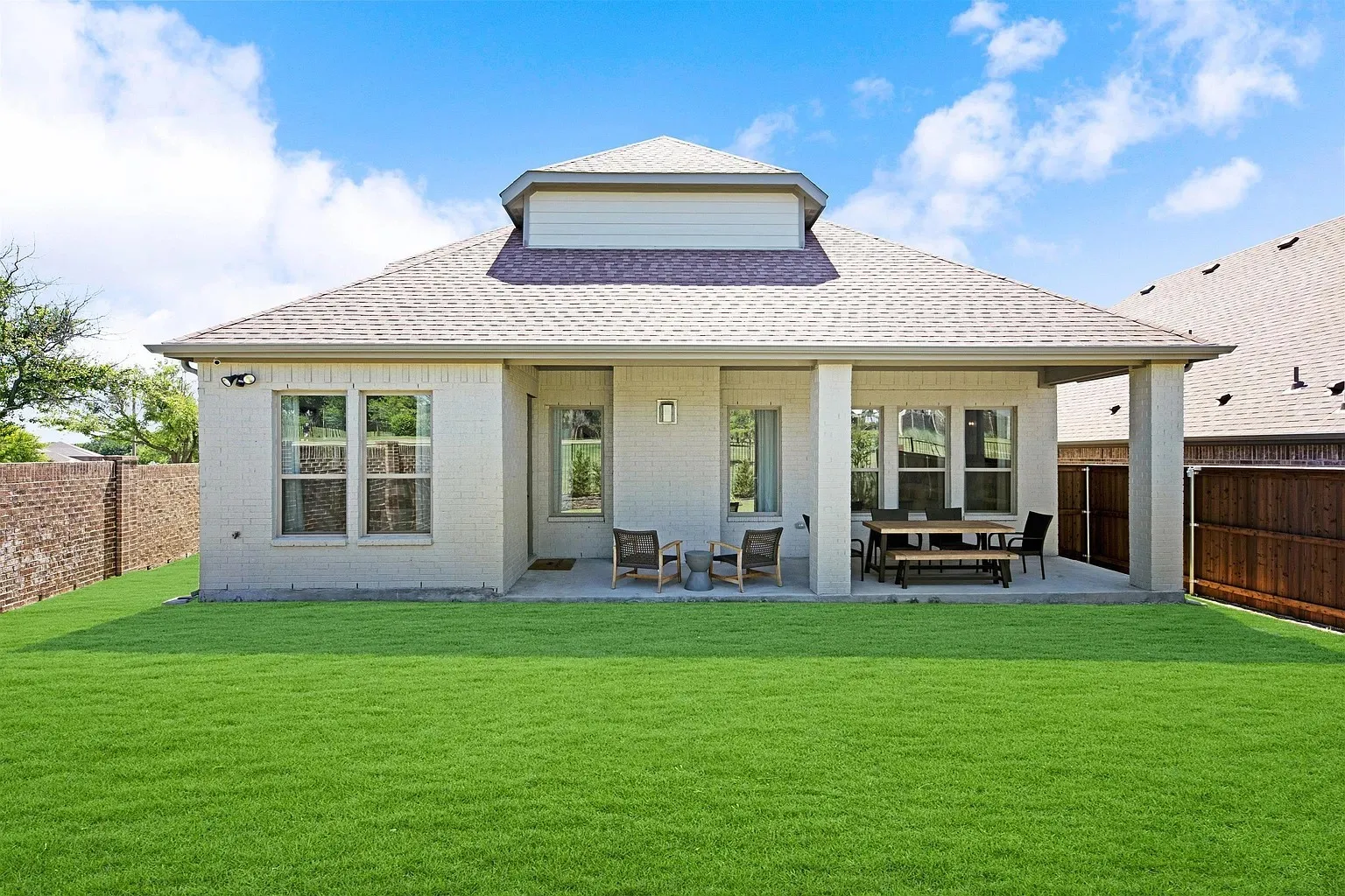 Expansive green lawn with a covered patio featuring substantial support columns, multiple windows, and a dormer architectural detail