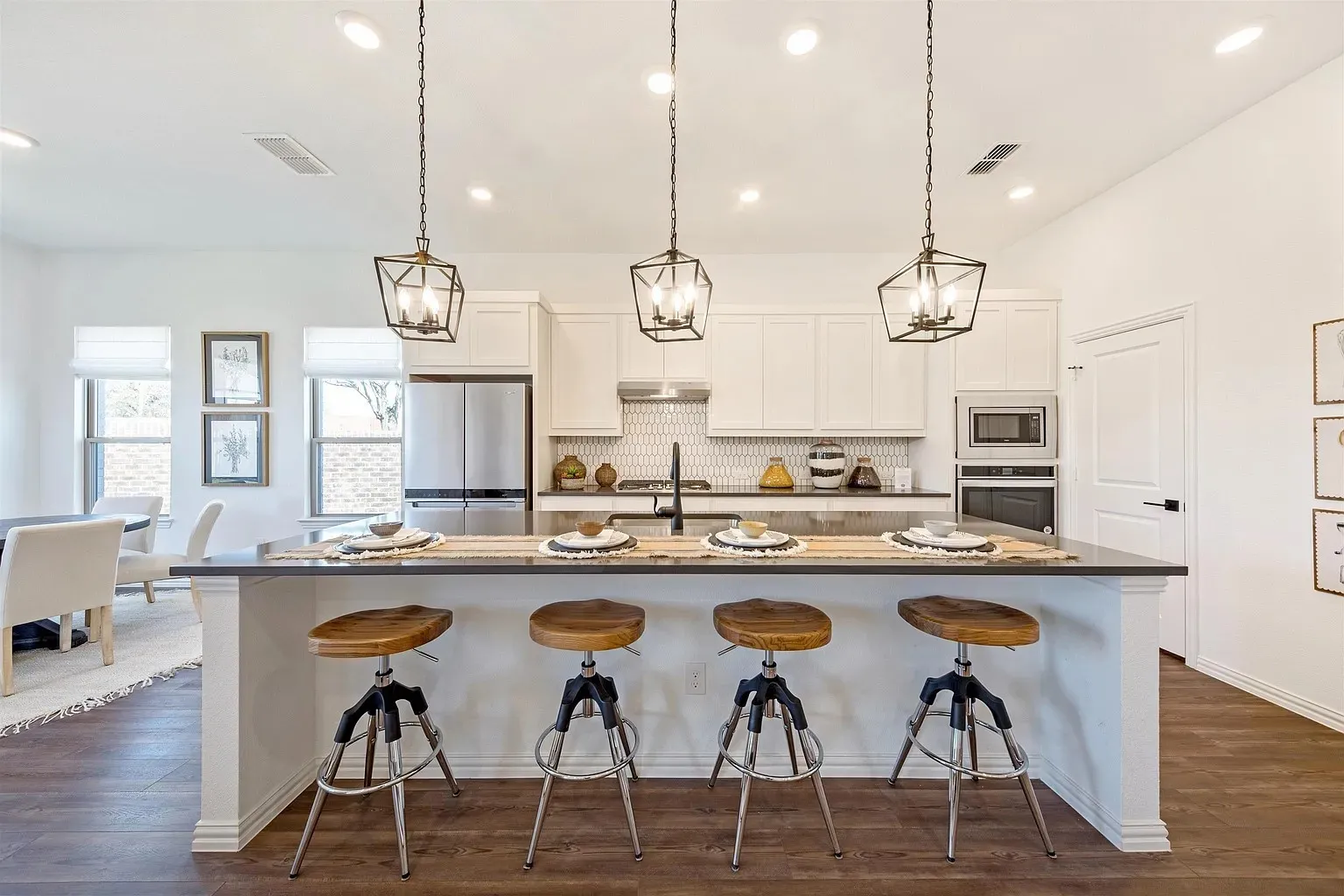 Spacious kitchen island with dark countertop, white shaker-style cabinetry, stainless steel appliances, and wood-finish flooring