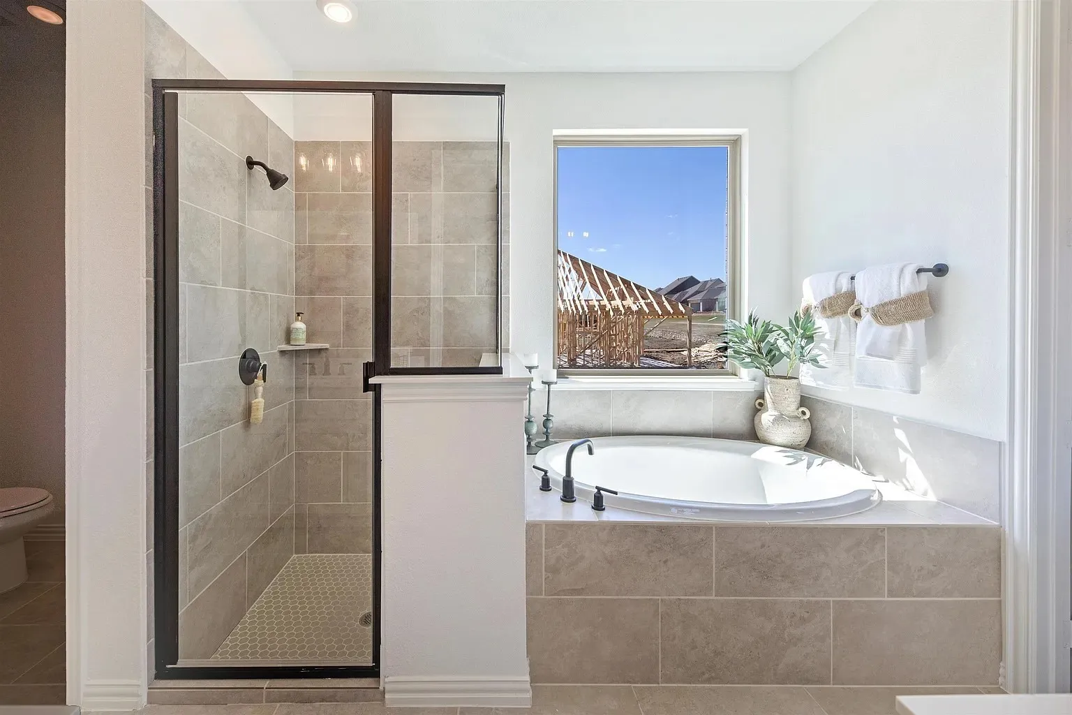 Tile-surround soaking tub with a black-finish faucet, accompanied by a glass-enclosed shower with black-finish fixtures