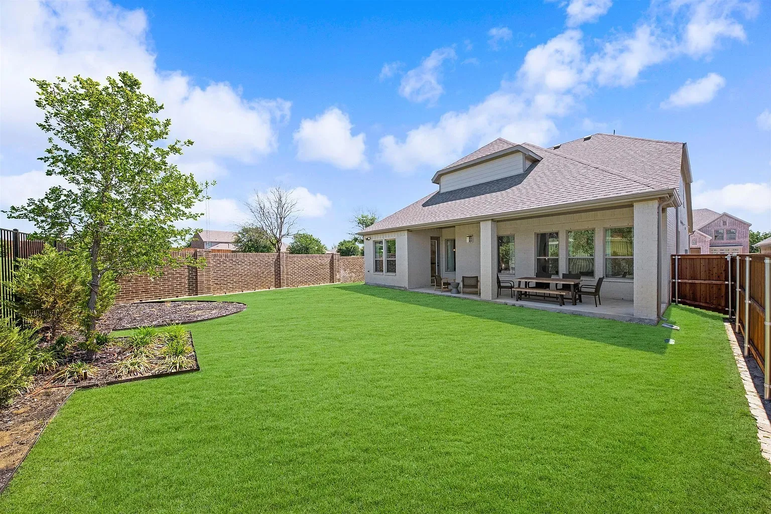Expansive green lawn, covered patio, brick privacy wall, wood fence, and mature landscaping