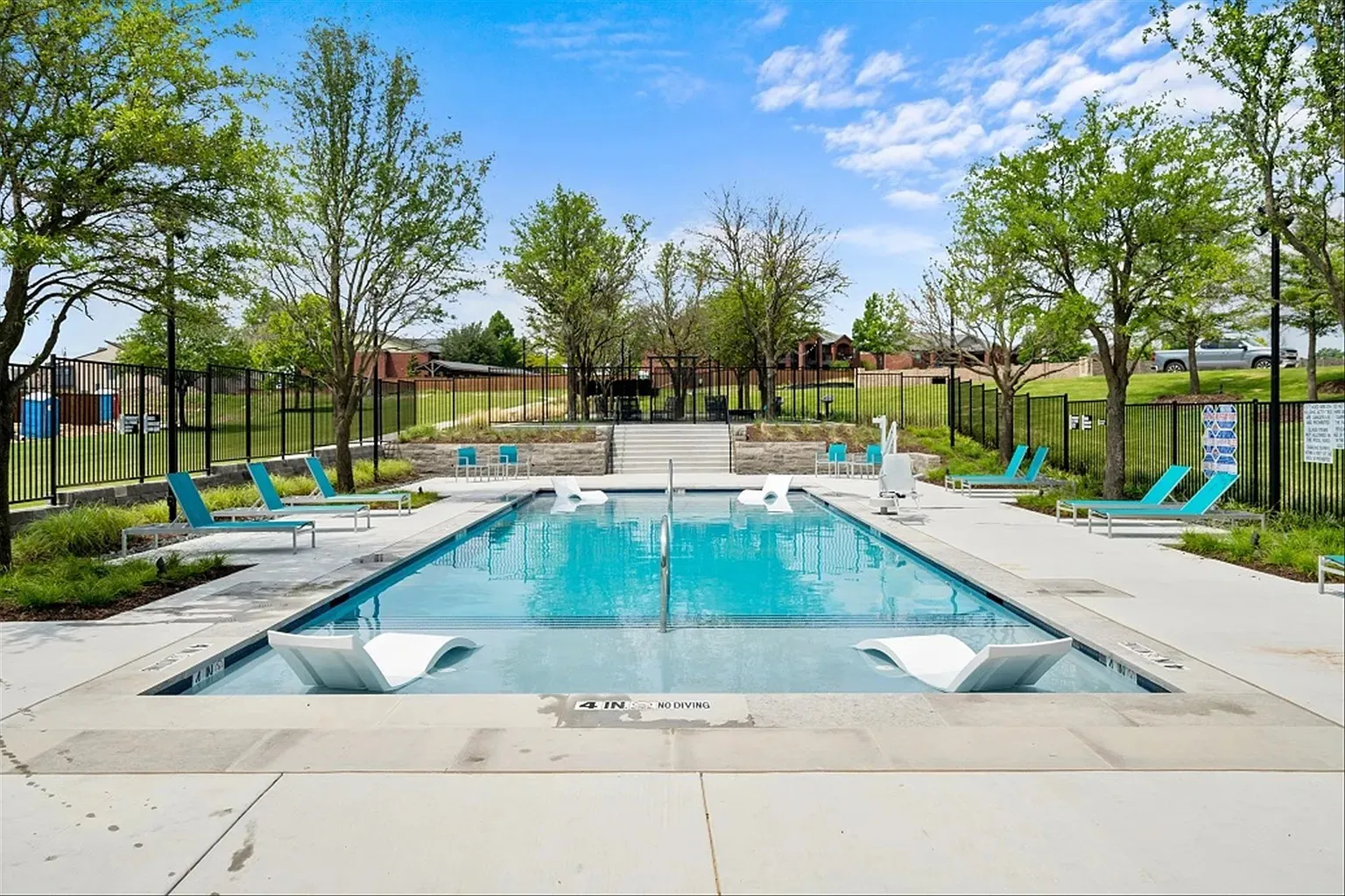 Rectangular swimming pool with integrated lounge seating, surrounded by concrete decking and a black metal fence