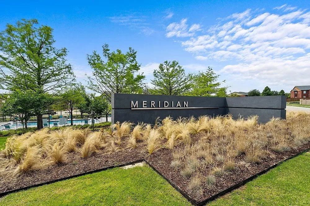 Community entry sign with a modern design, surrounded by a landscaped bed of ornamental grasses and mulch