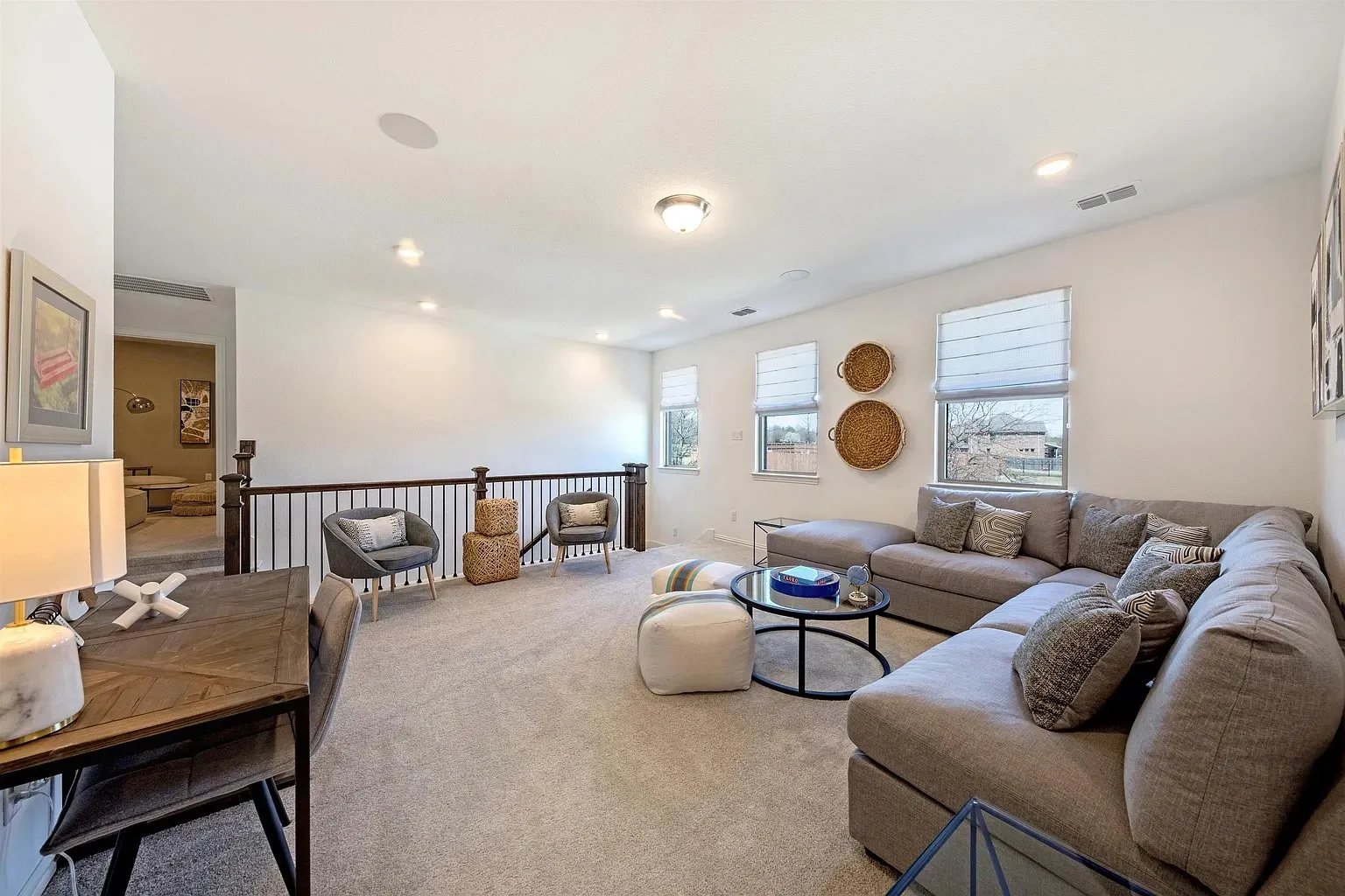 Carpeted recreation room with recessed lighting, multiple windows, and a dark wood and metal baluster railing