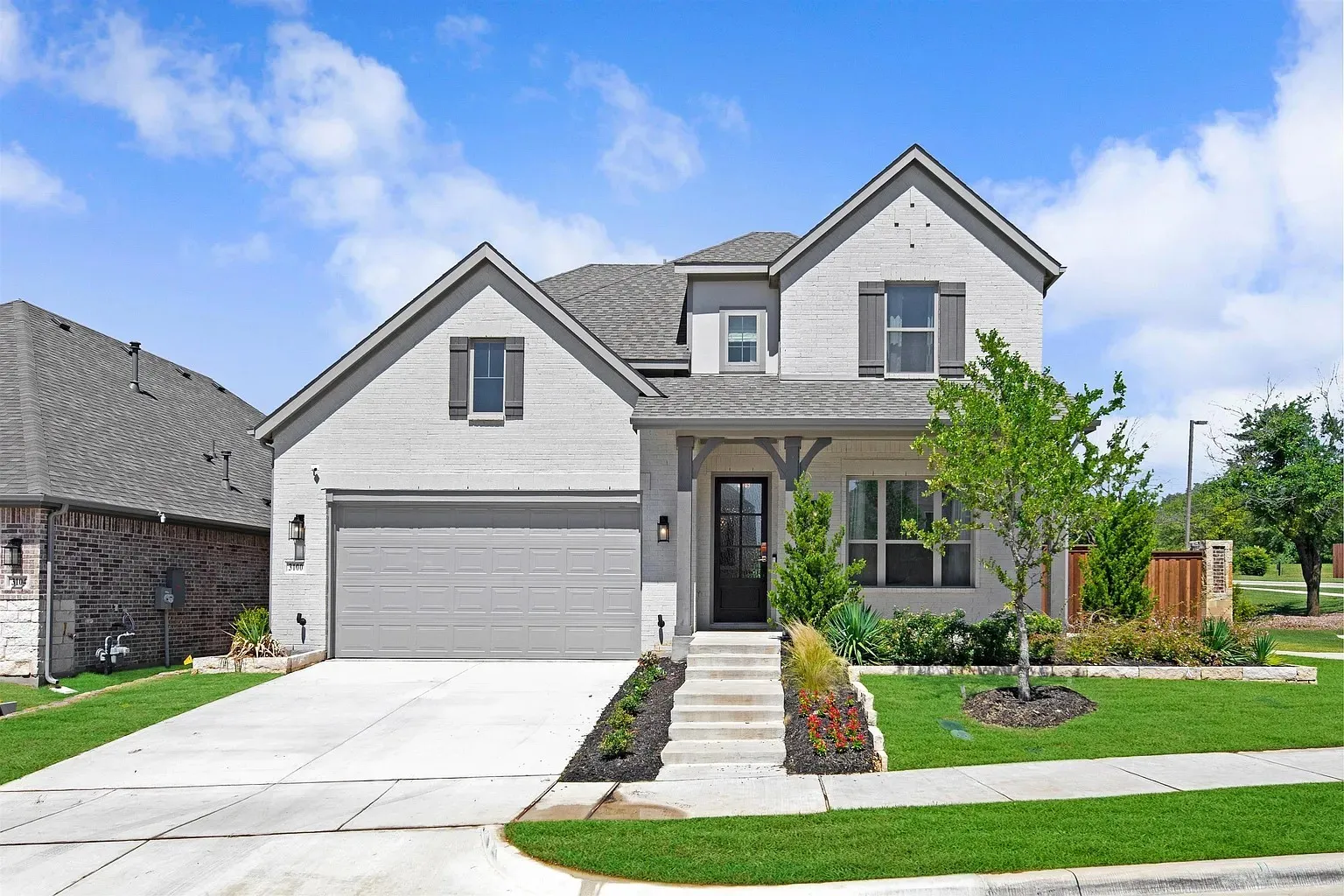Contemporary exterior with light-colored brick, dark shutters, an attached garage, a covered front entry, and a manicured lawn