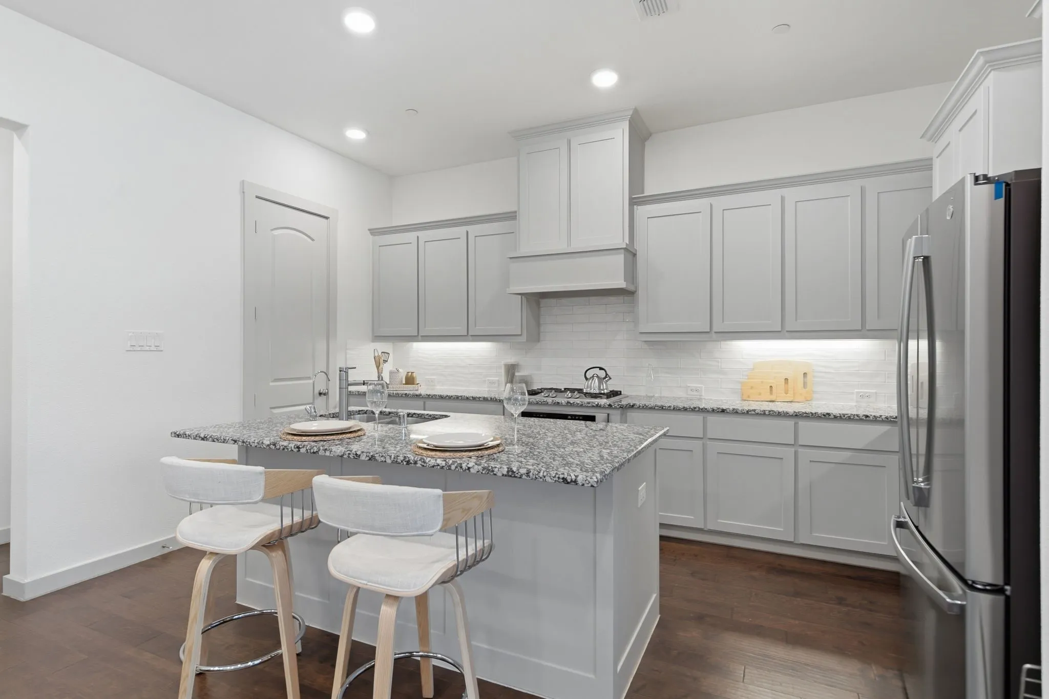 Kitchen featuring a central island with a stone countertop, light grey cabinetry, stainless steel appliances, wood-finish flooring, and recessed lighting