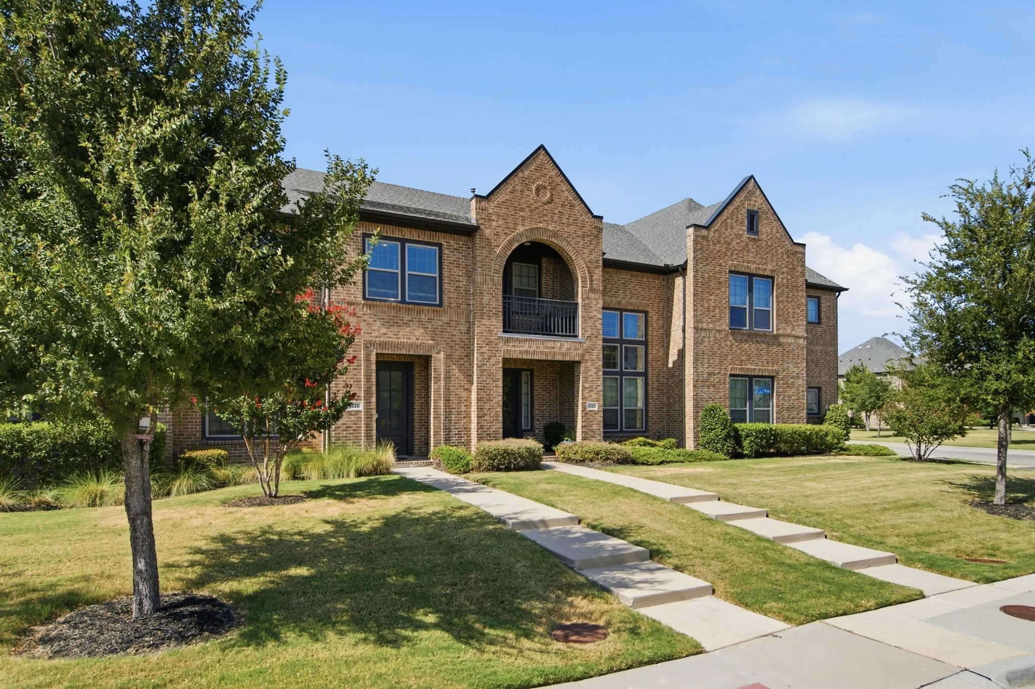 Traditional-style brick townhouse featuring a covered entry balcony with wrought iron railing, arched entryway, multi-pane windows, and a gabled roofline