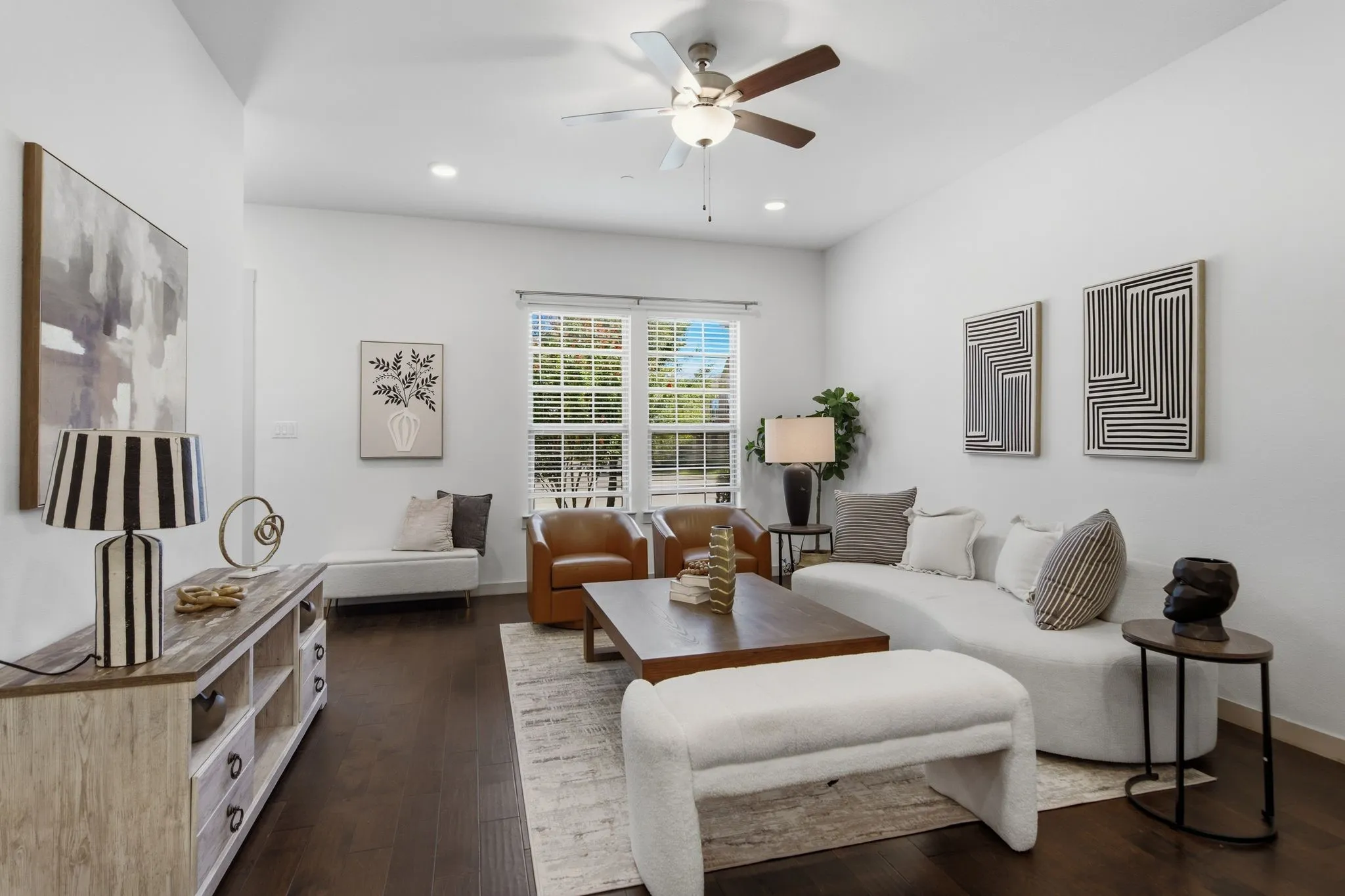 Spacious living area featuring dark wood-finish flooring, white walls, and a ceiling fan with integrated lighting