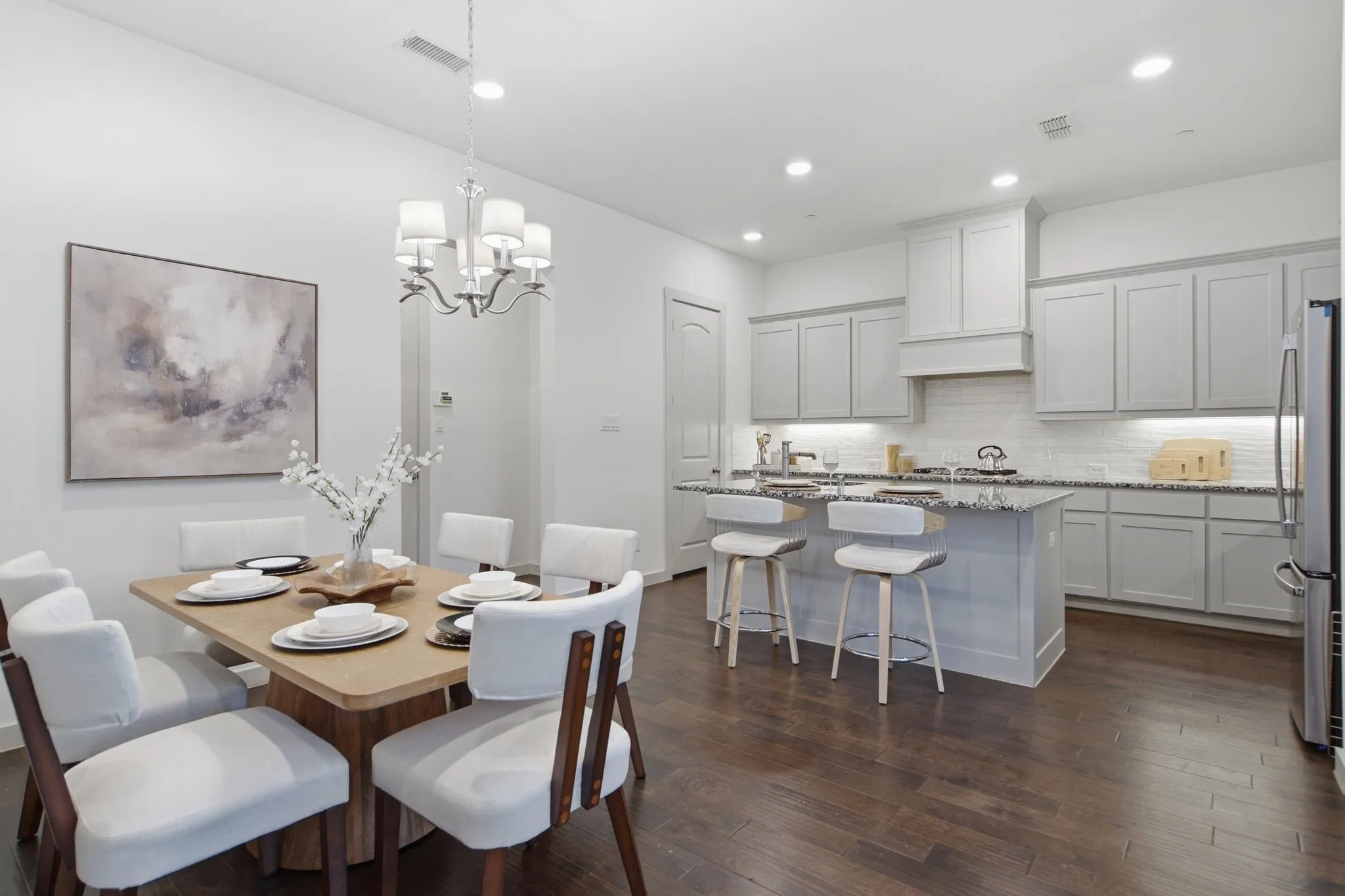 Open-concept dining and kitchen area featuring dark wood-finish flooring, light grey cabinetry, a kitchen island with seating, a white subway tile backsplash, and recessed lighting