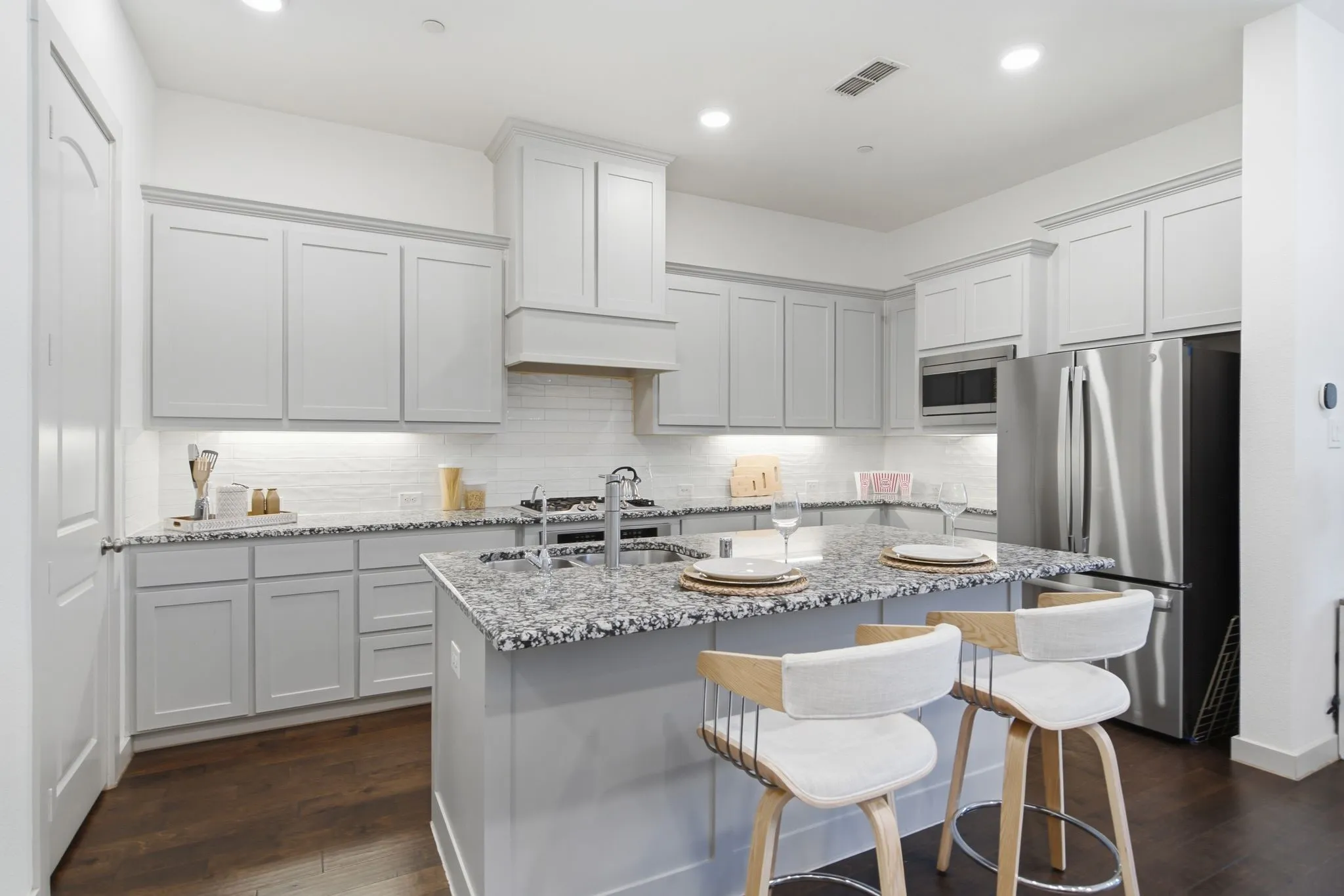 Modern kitchen featuring light gray cabinetry, a central island with countertop seating, stainless steel appliances, a white subway tile backsplash, and dark wood-finish flooring