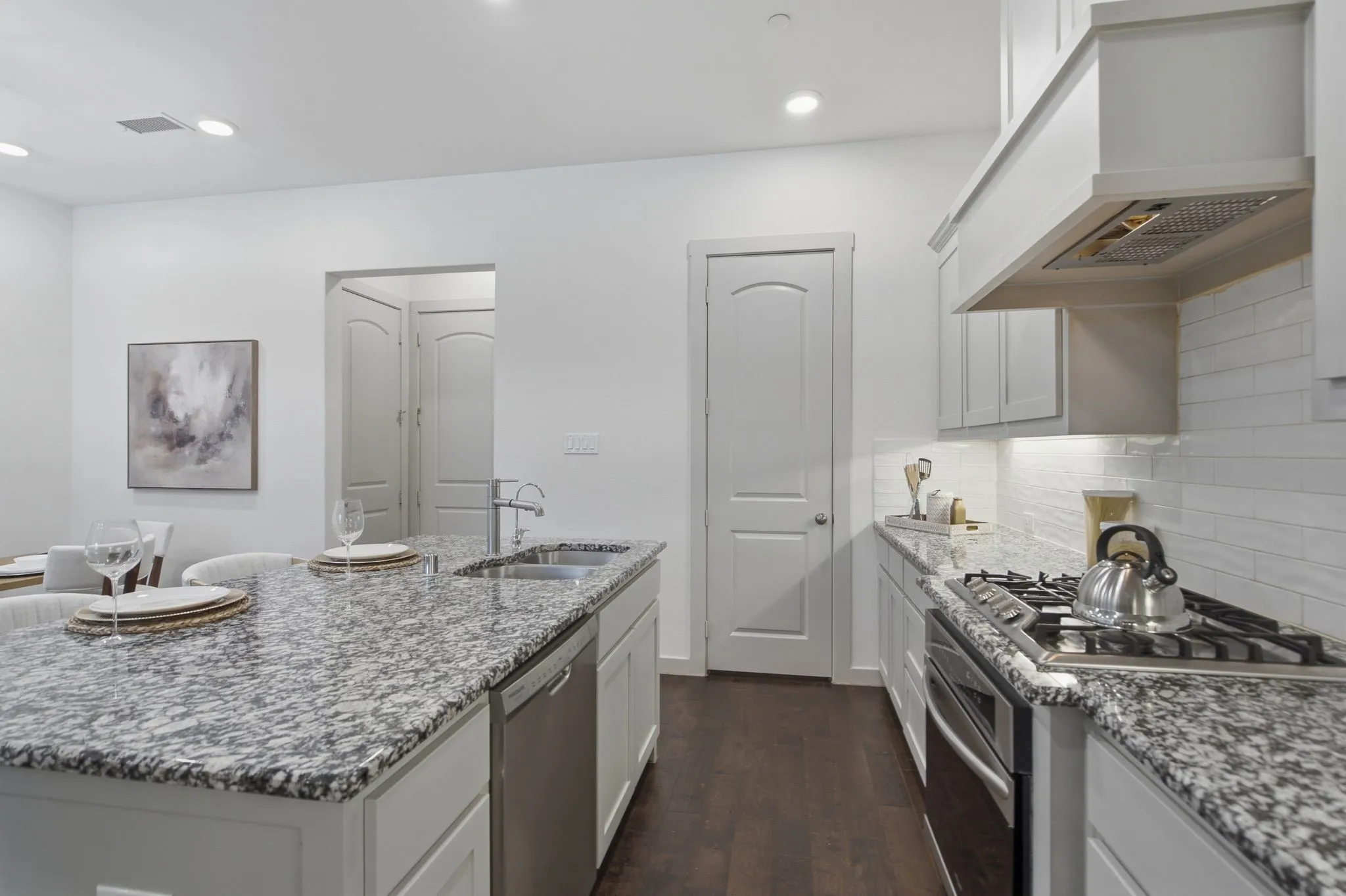 Open-concept kitchen featuring an oversized island with double-basin stainless steel sink, granite countertops, and built-in dishwasher