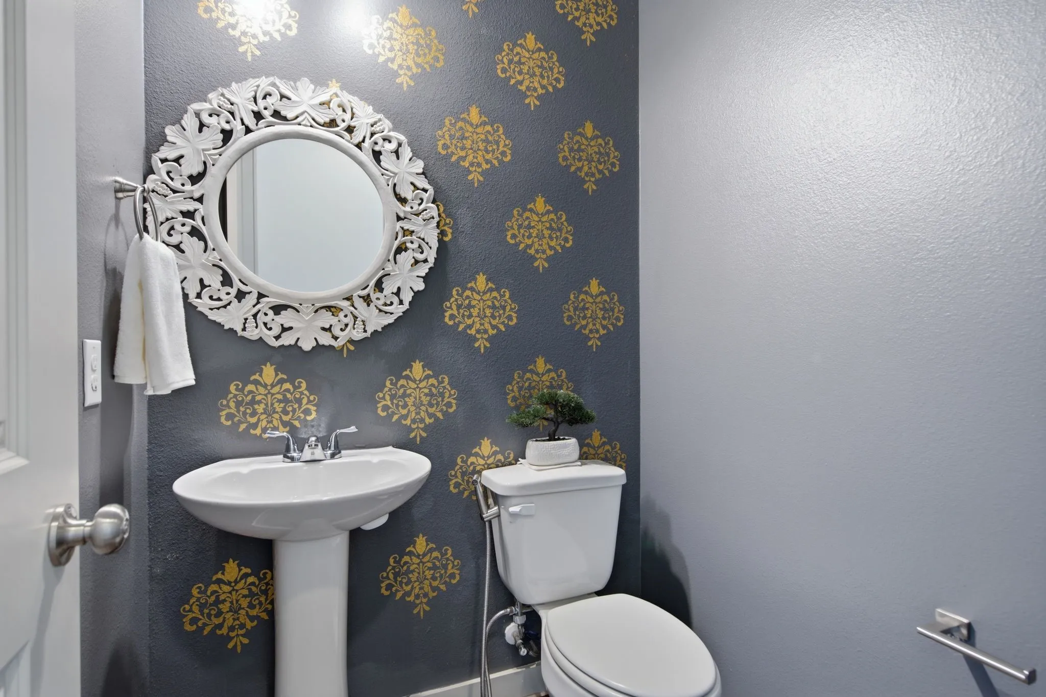 Powder room with a decorative accent wall, featuring a pedestal sink, a toilet, and a white carved-frame mirror