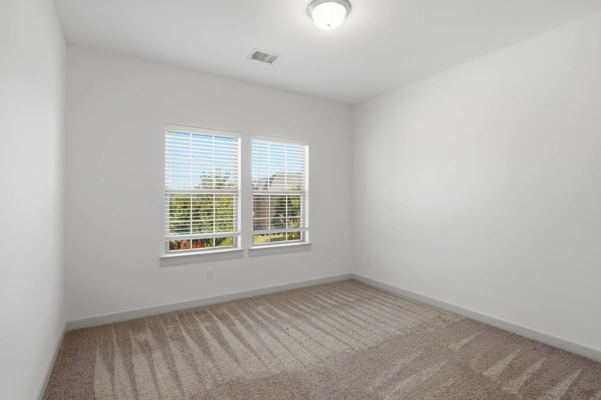 Room featuring light neutral carpeting, white walls, and two windows with blinds