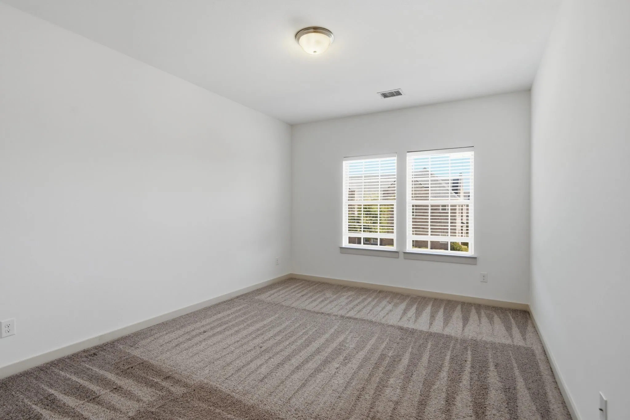 Bright interior space featuring dual windows with blinds, neutral carpeting, and a flush-mount ceiling light fixture