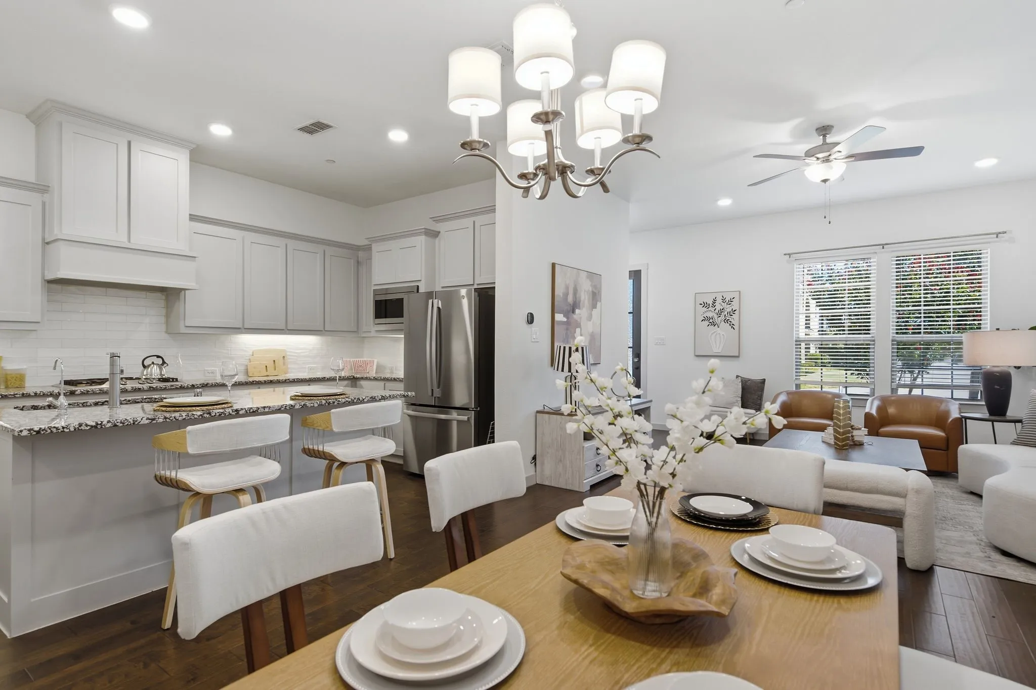 Open-concept living area featuring wood-finish flooring, a contemporary chandelier, a kitchen island with seating, stainless steel appliances, and white cabinetry