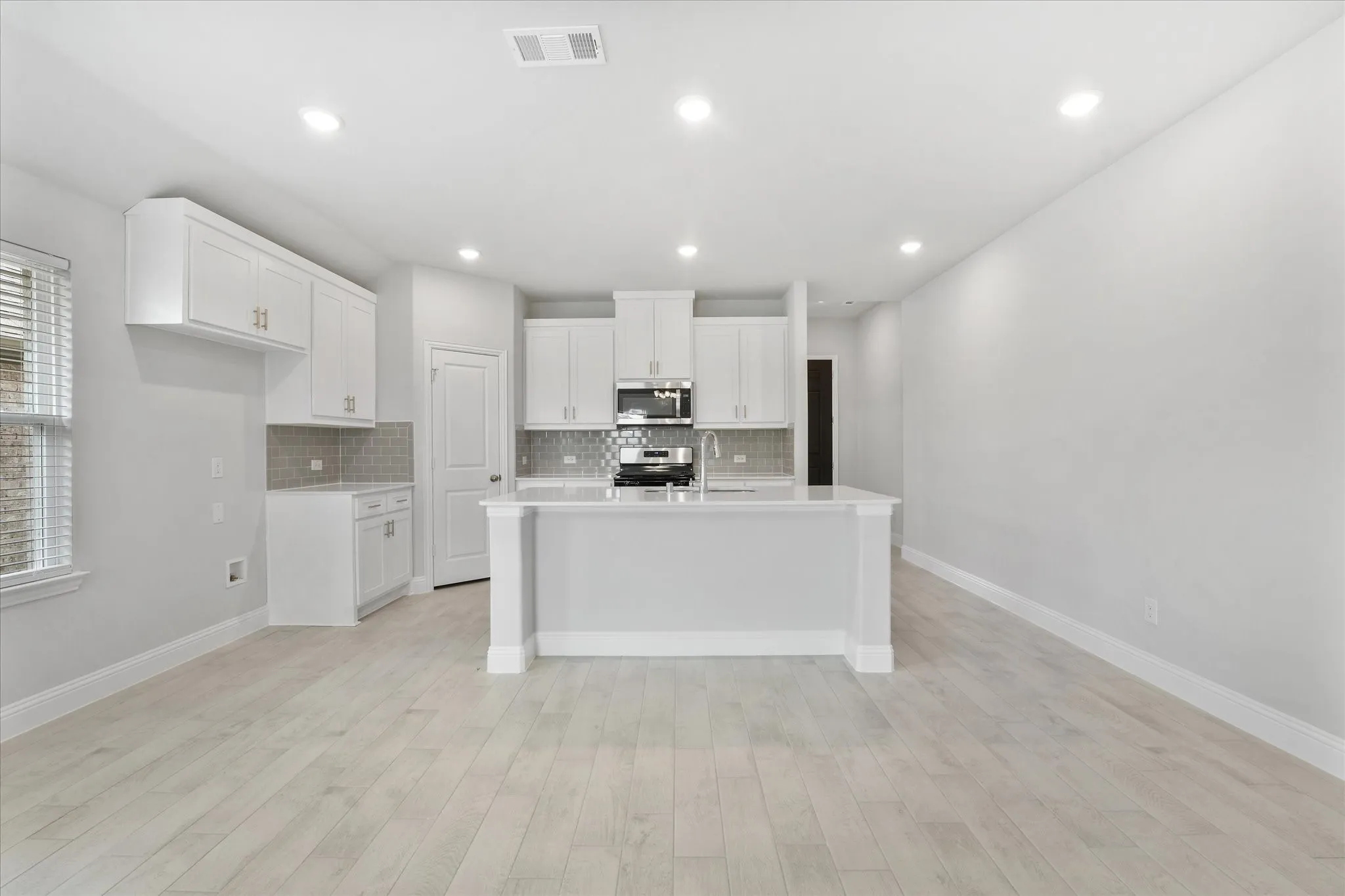 Kitchen with range, light hardwood / wood-style flooring, tasteful backsplash, white cabinets, and a kitchen island with sink