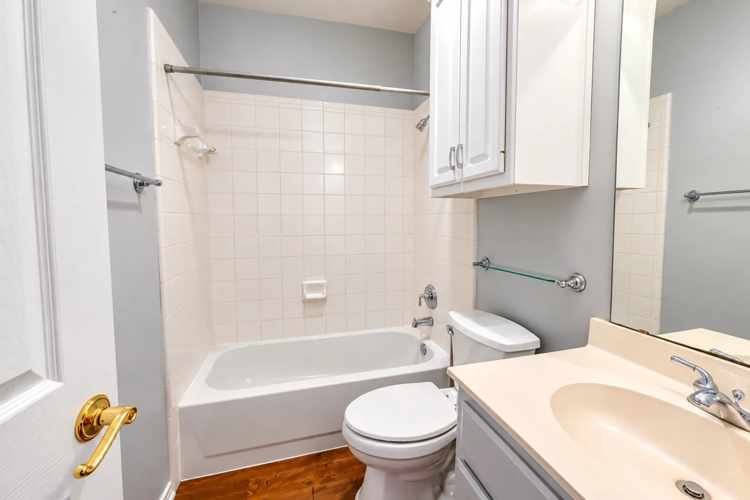 Bathroom featuring a shower-tub combination with white tile surround, wood-finish flooring, a single vanity with a solid surface countertop, and white cabinetry