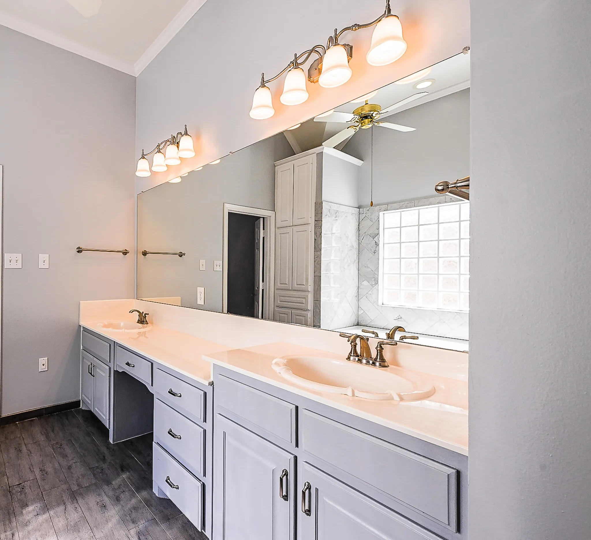 Dual vanity with integrated sinks, extensive counter space, custom cabinetry, wood-finish flooring, and a large wall-mounted mirror