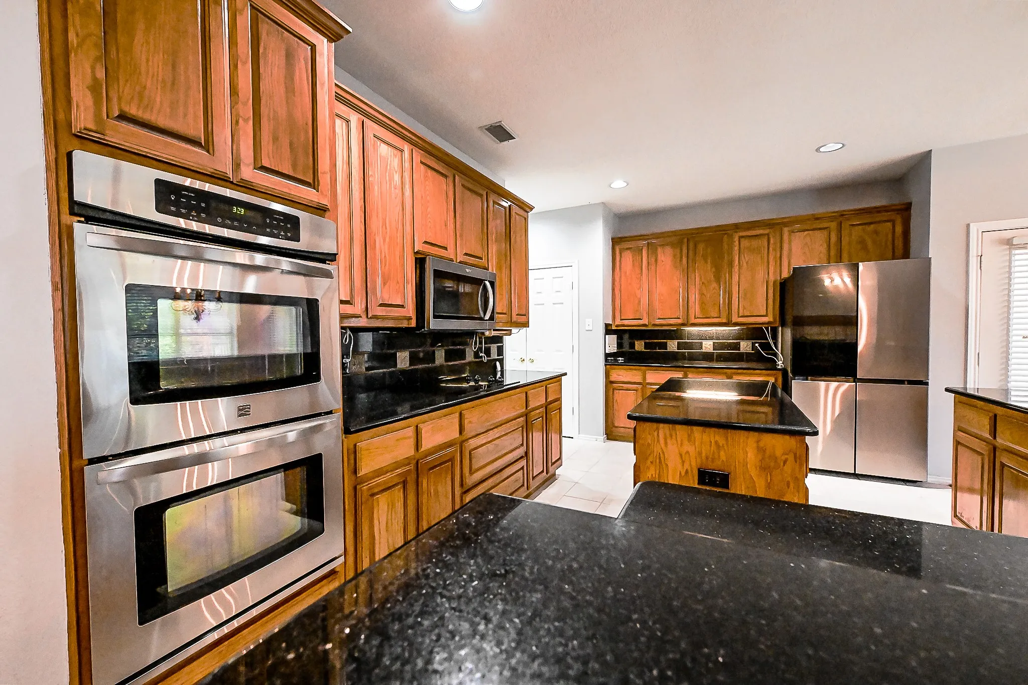 Kitchen featuring wood cabinetry, dark countertops, stainless steel double ovens, a built-in microwave, and a stainless steel refrigerator