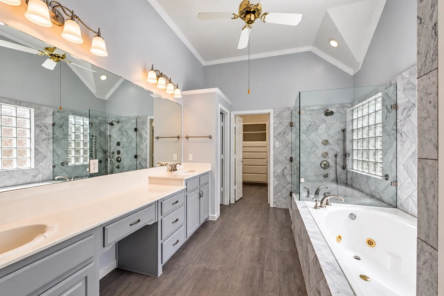 Vaulted ceiling with a ceiling fan, dual vanity with extensive counter space, separate soaking tub, and a glass-enclosed shower with multiple shower heads