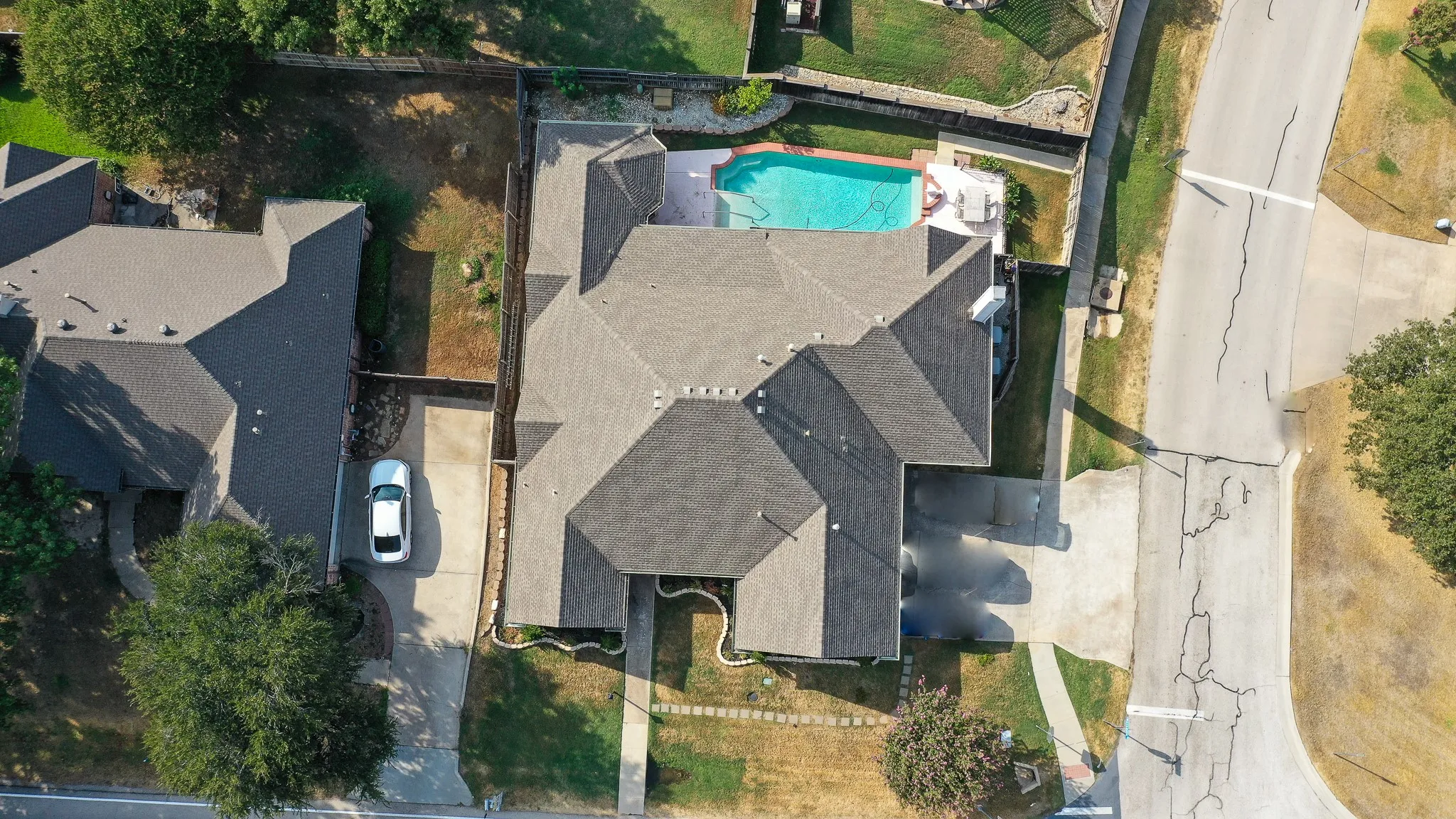 Aerial perspective highlighting the property with a private pool, extensive paved driveway, and established landscaping