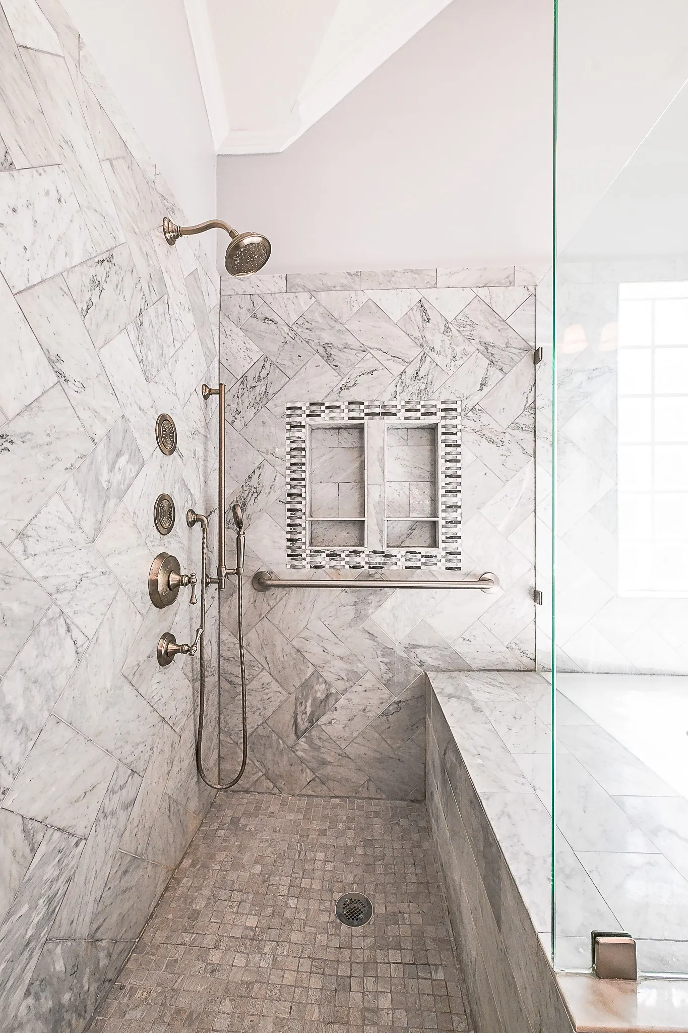 Glass-enclosed shower with full-height marble-finish tile, mosaic tile accents, a built-in bench, and a rainfall showerhead