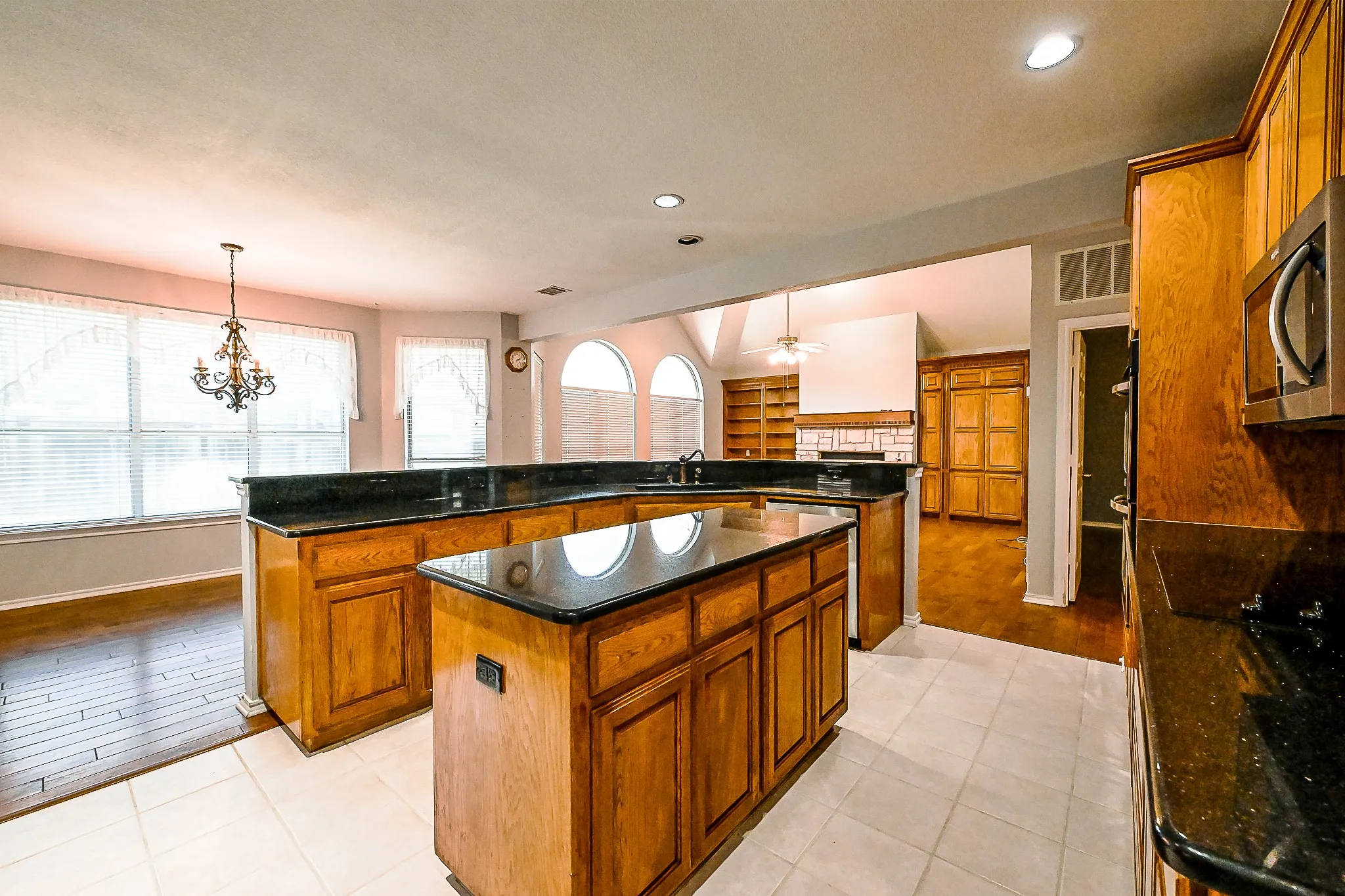 Kitchen featuring a central island, dark countertops, wood-finish cabinetry, built-in microwave, and tile flooring