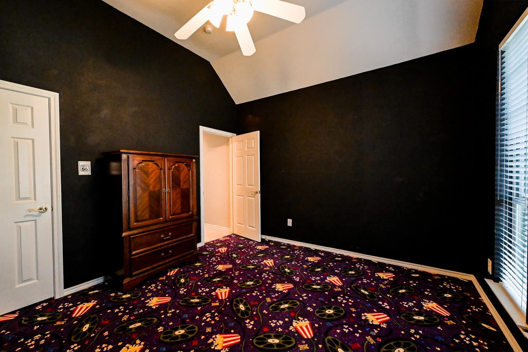 Vaulted ceiling with a ceiling fan, dark painted walls, pattern carpet flooring, and window with blinds