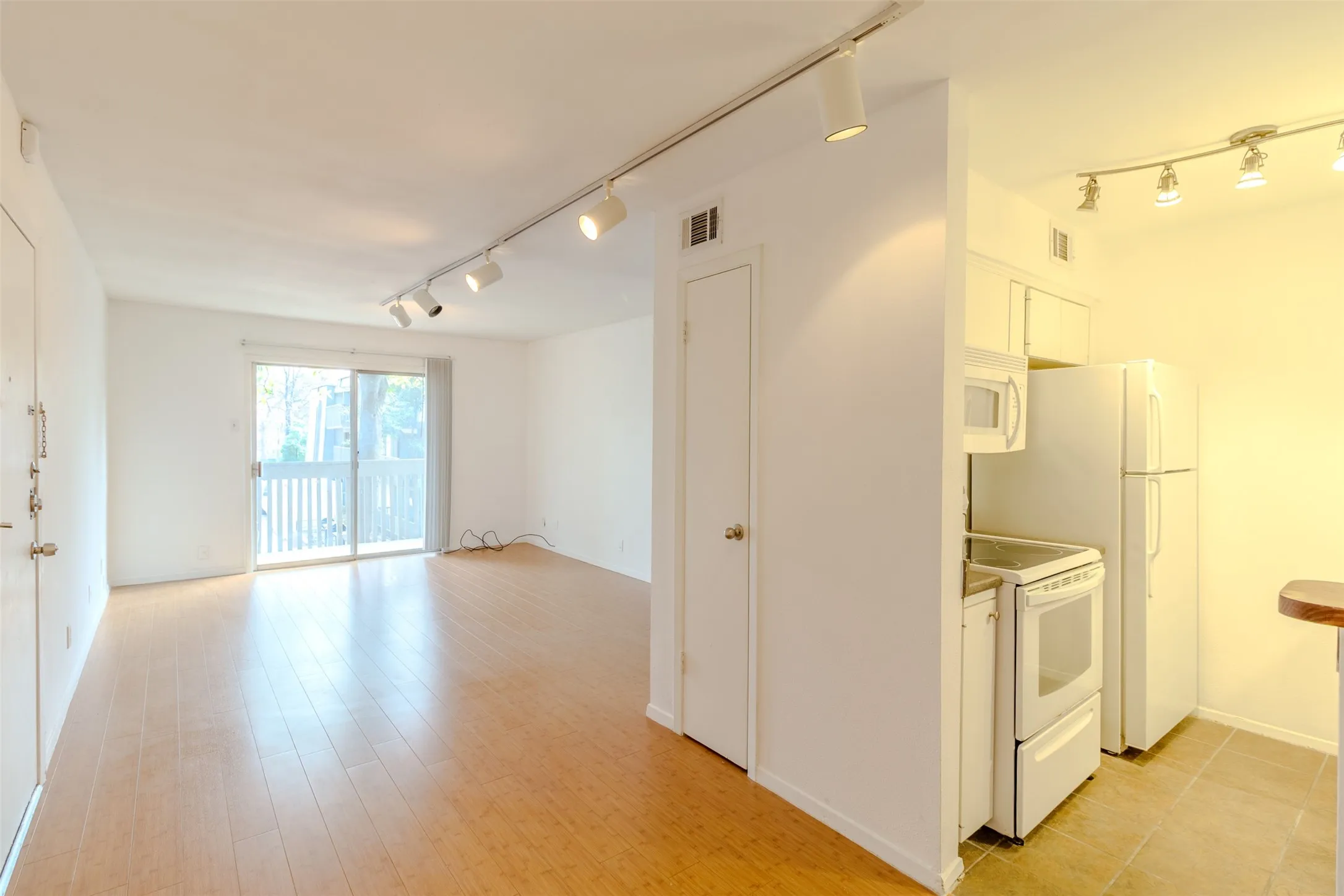 Kitchen featuring white appliances, track lighting, white cabinetry, light wood-style flooring, and light countertops