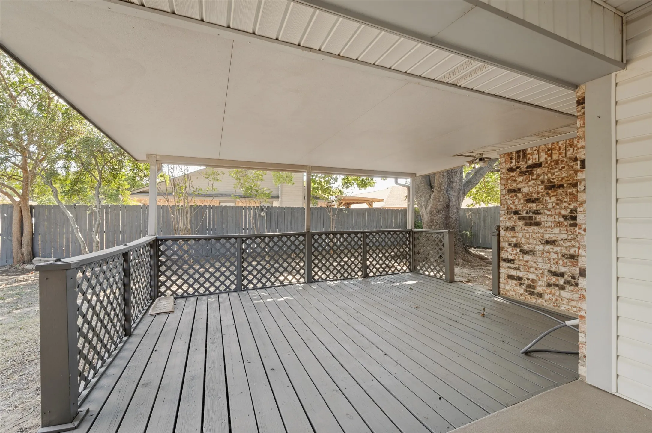 Covered deck with painted wood flooring and lattice railing, alongside a brick exterior wall.