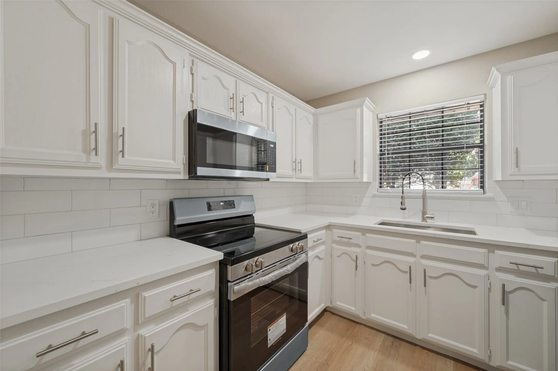 White cabinetry with brushed nickel hardware, white subway tile backsplash, white quartz countertops, built-in stainless steel microwave, and stainless steel electric range