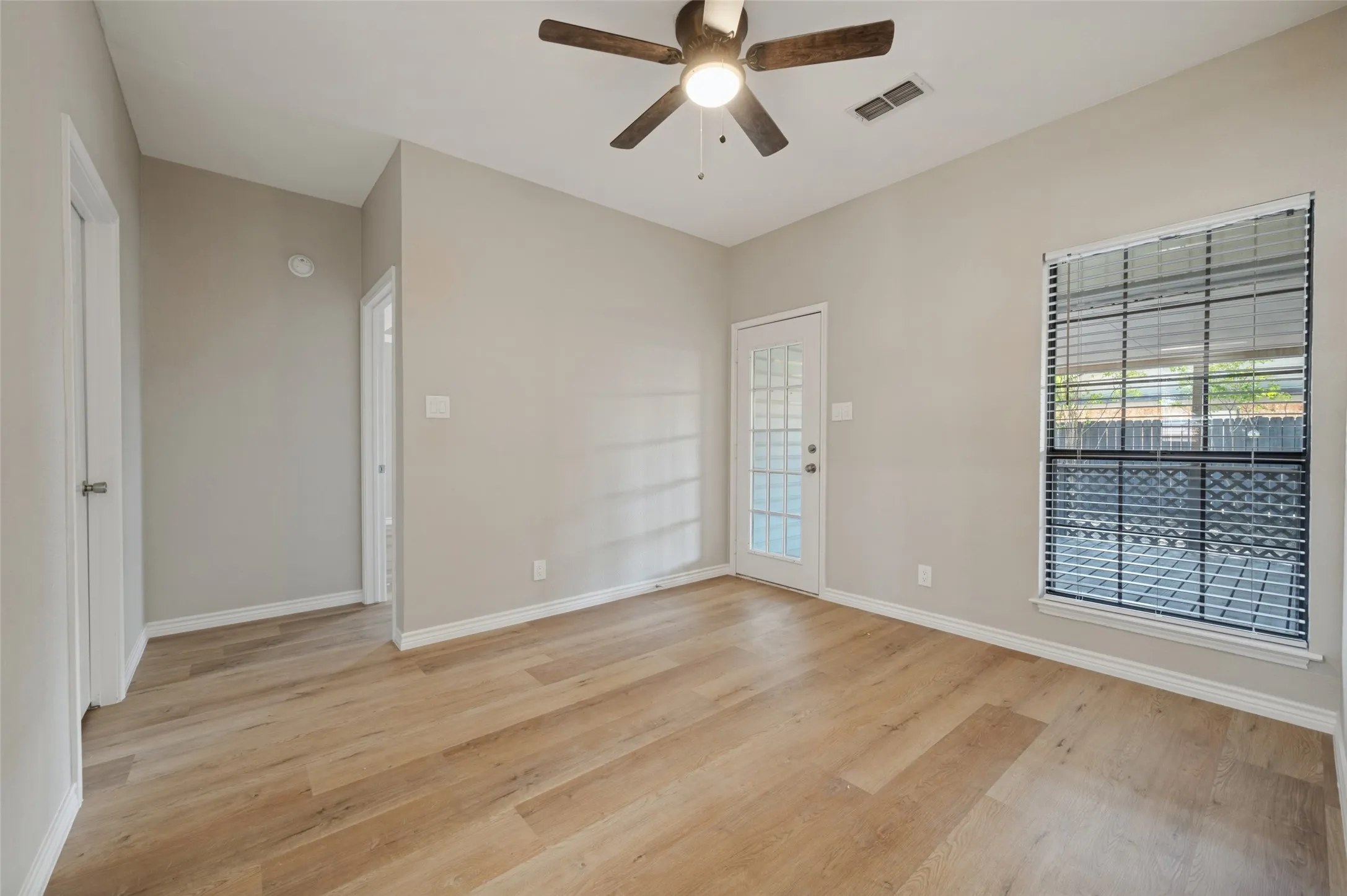 LVP flooring, neutral wall color, ceiling fan with integrated lighting, window with blinds, and white door with glass panels