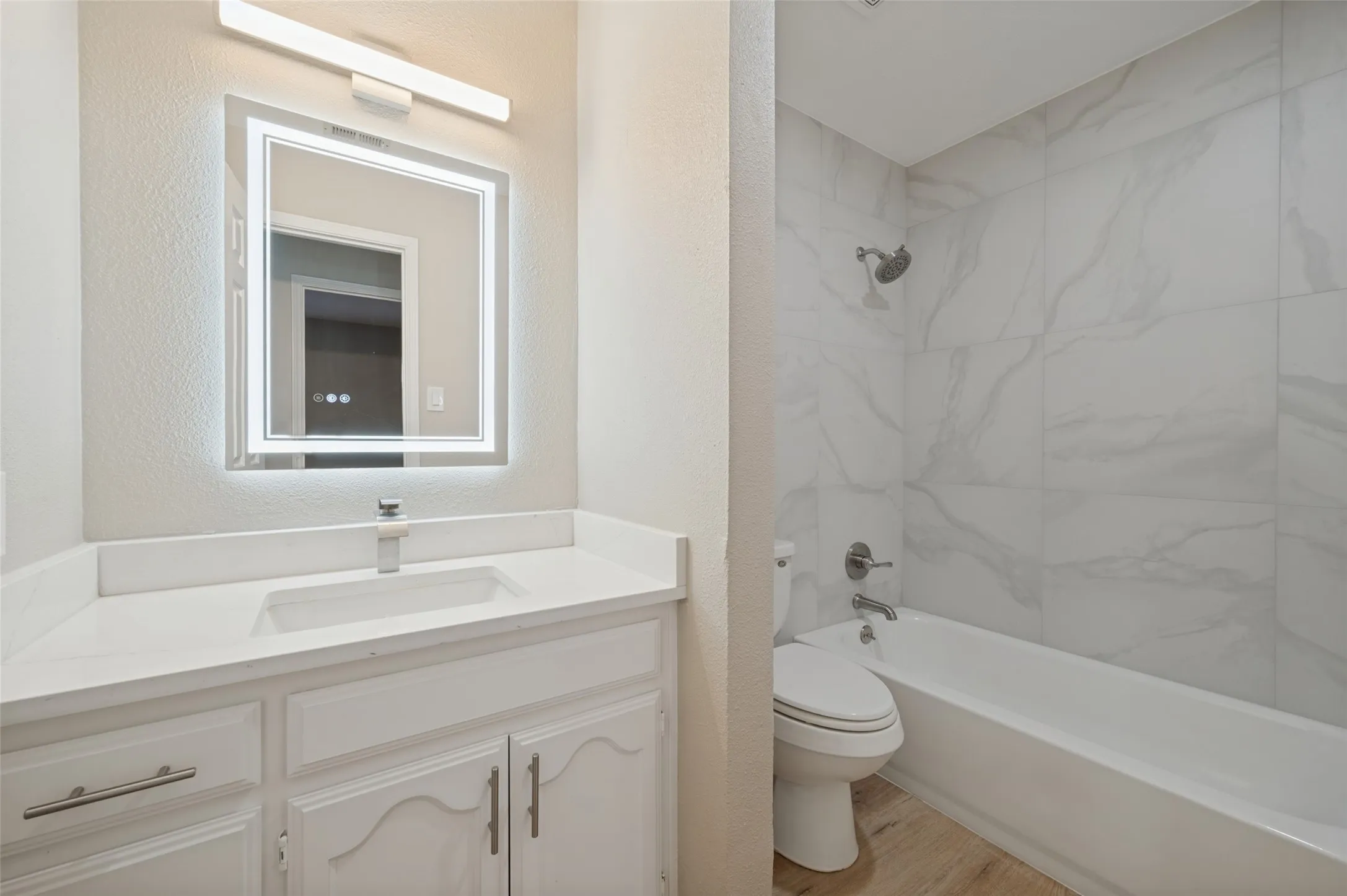 Vanity with a white countertop and integrated sink, illuminated mirror, white cabinetry, and LVP flooring
